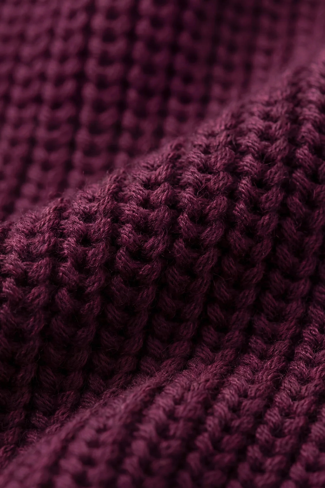 Close-up of a dark plum purple chunky knit fabric texture with soft folds and ribbed details.