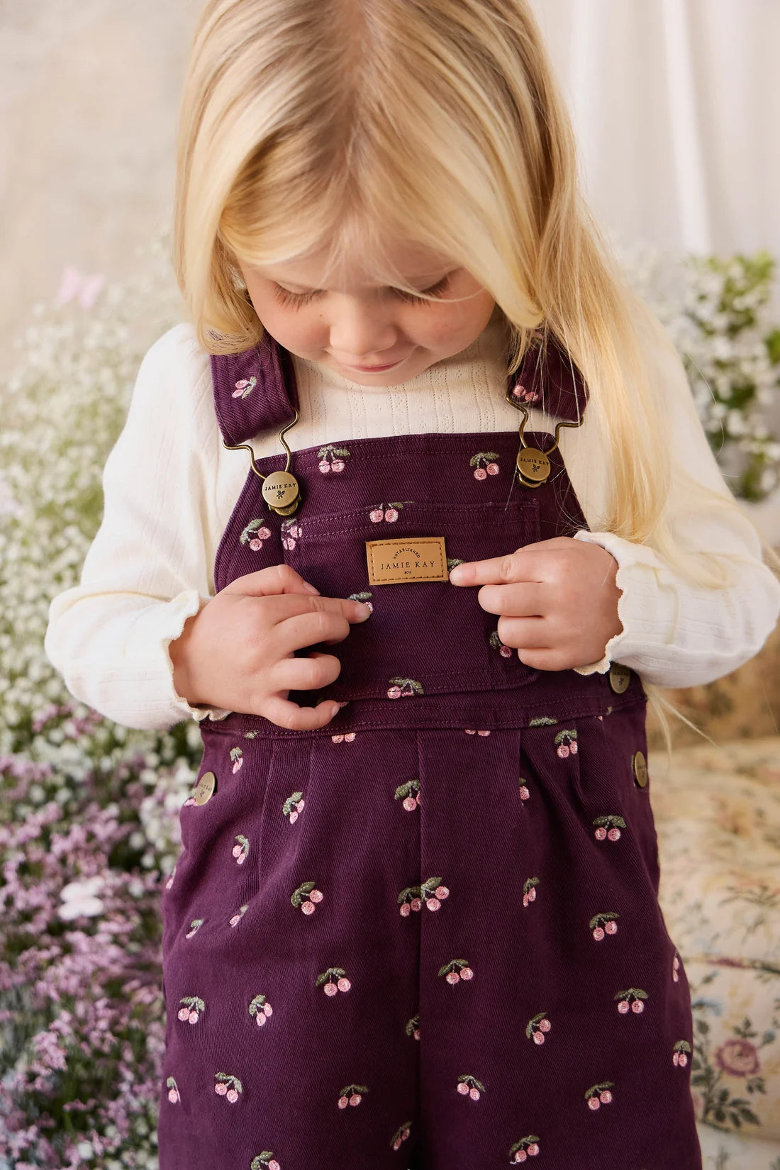 Young girl wearing a purple dress with cherry pattern, standing in a garden.