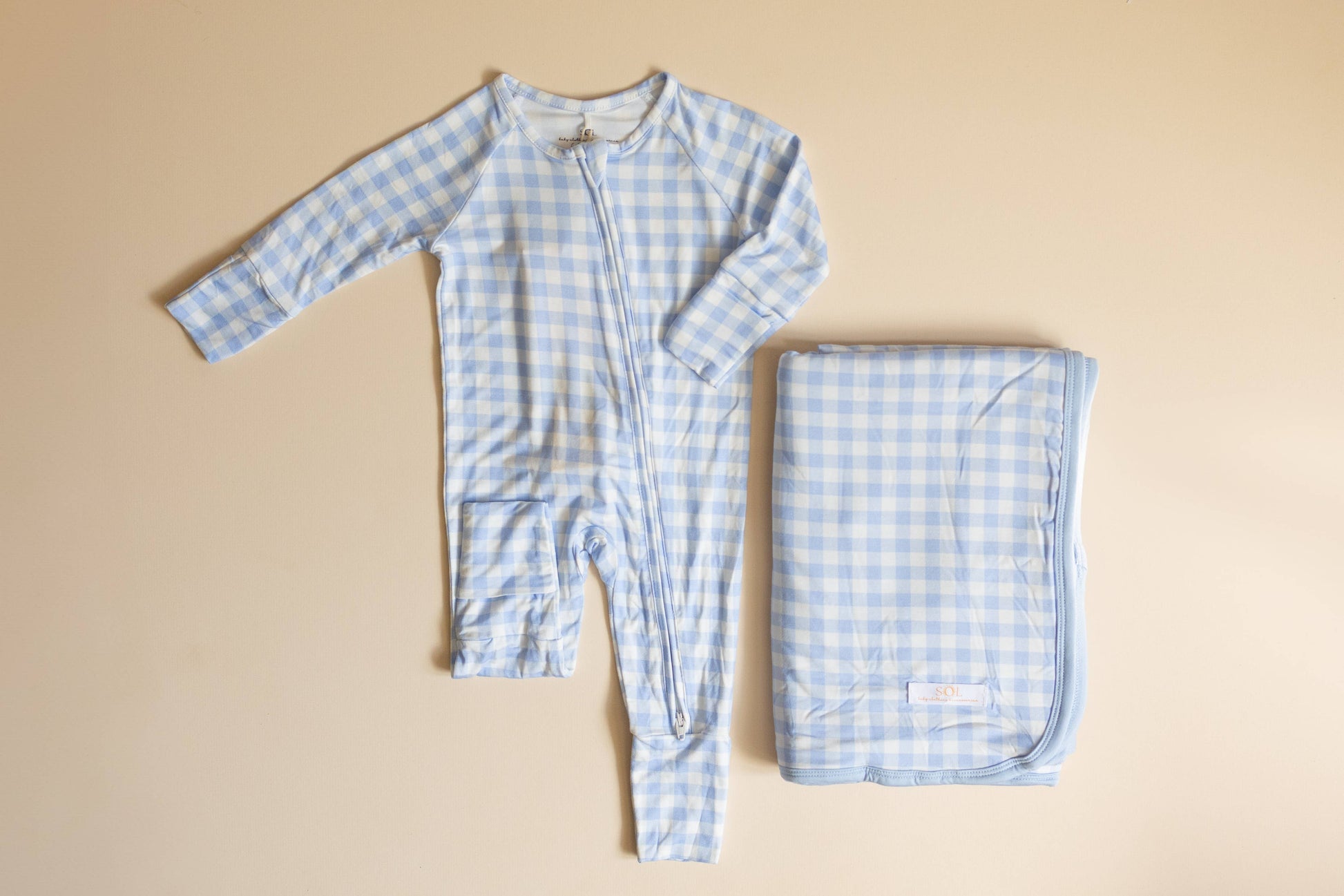 Blue checkered baby onesie and blanket on a beige background