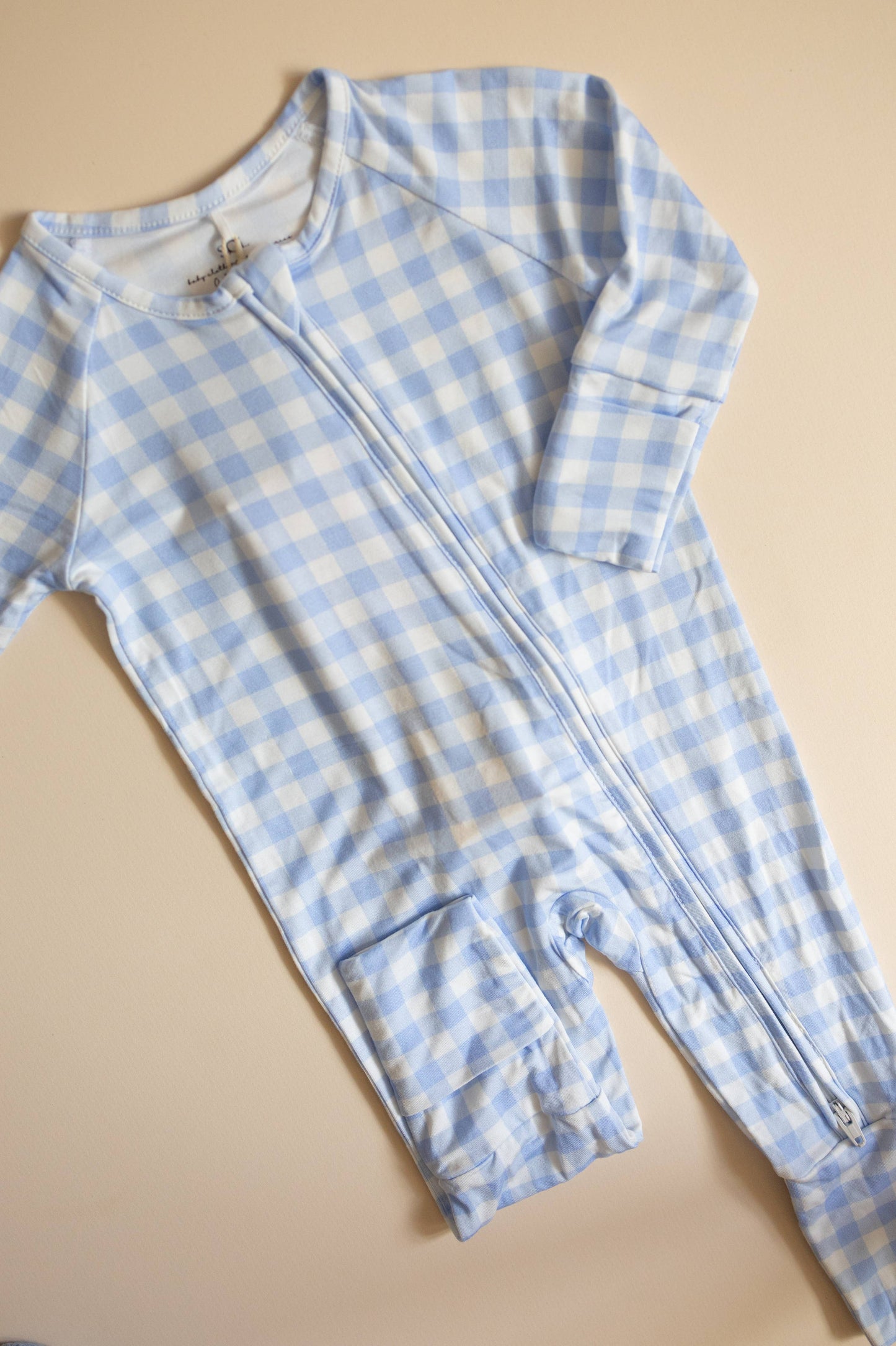 Blue and white checkered baby onesie with a zipper on a beige background