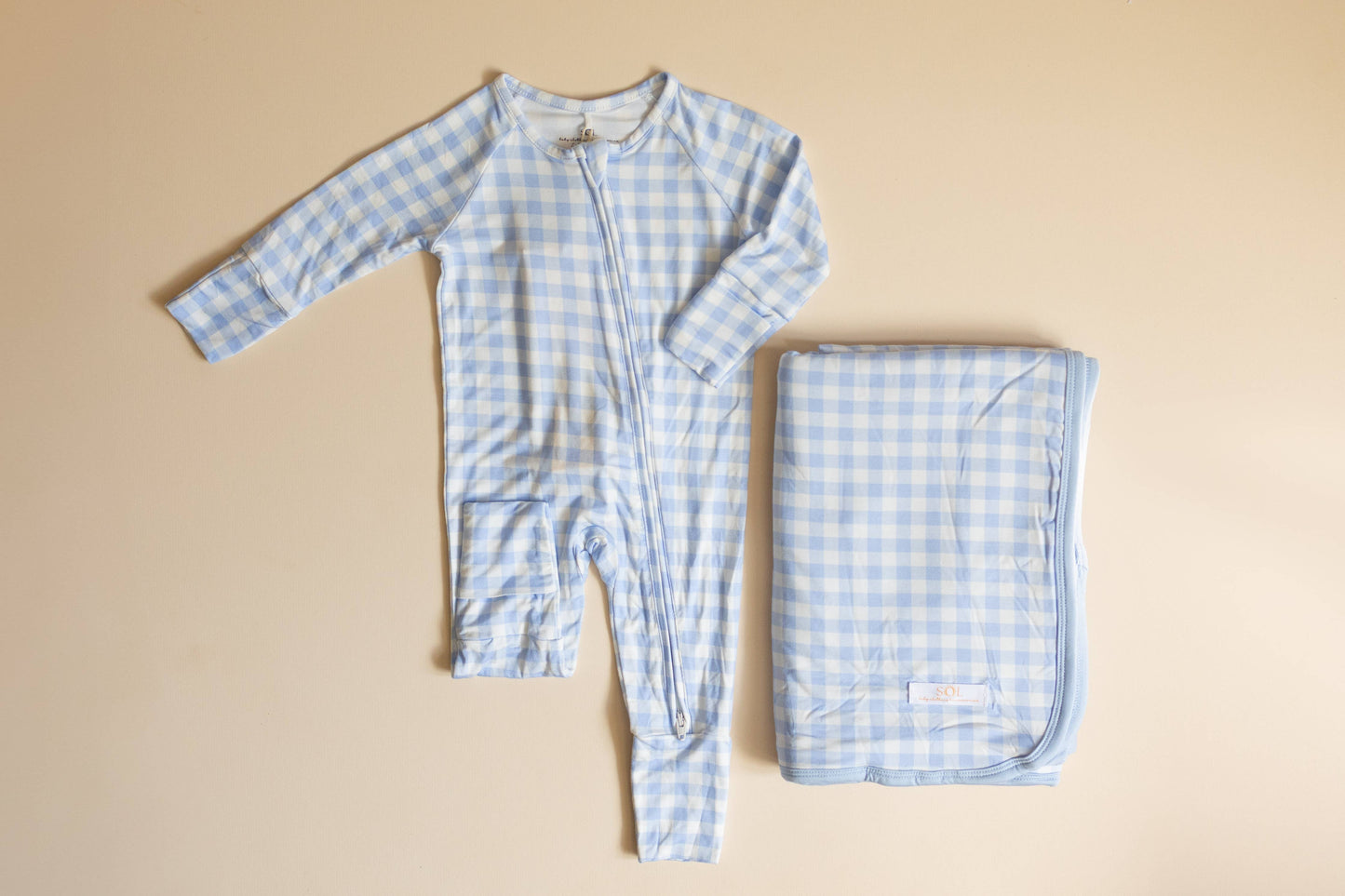 Blue checkered baby onesie and blanket on a beige background