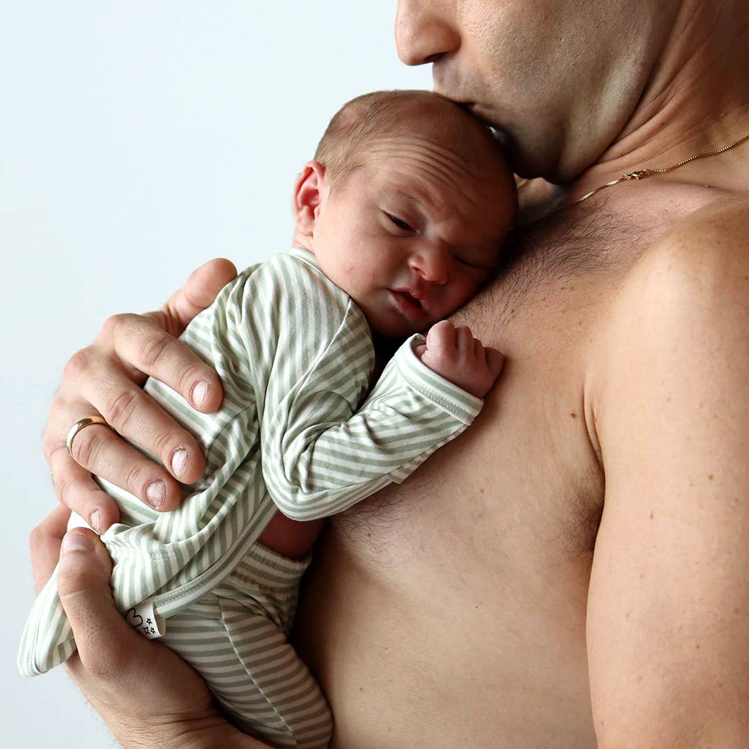 Newborn baby in a green and white striped outfit being held by an adult against a light background