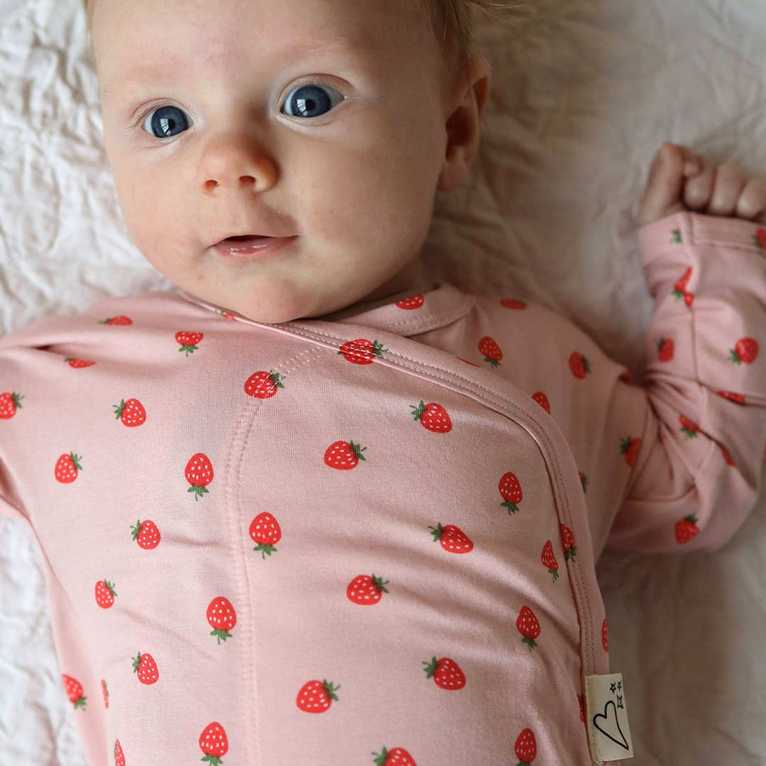 Baby wearing a pink outfit with strawberry pattern on a white blanket