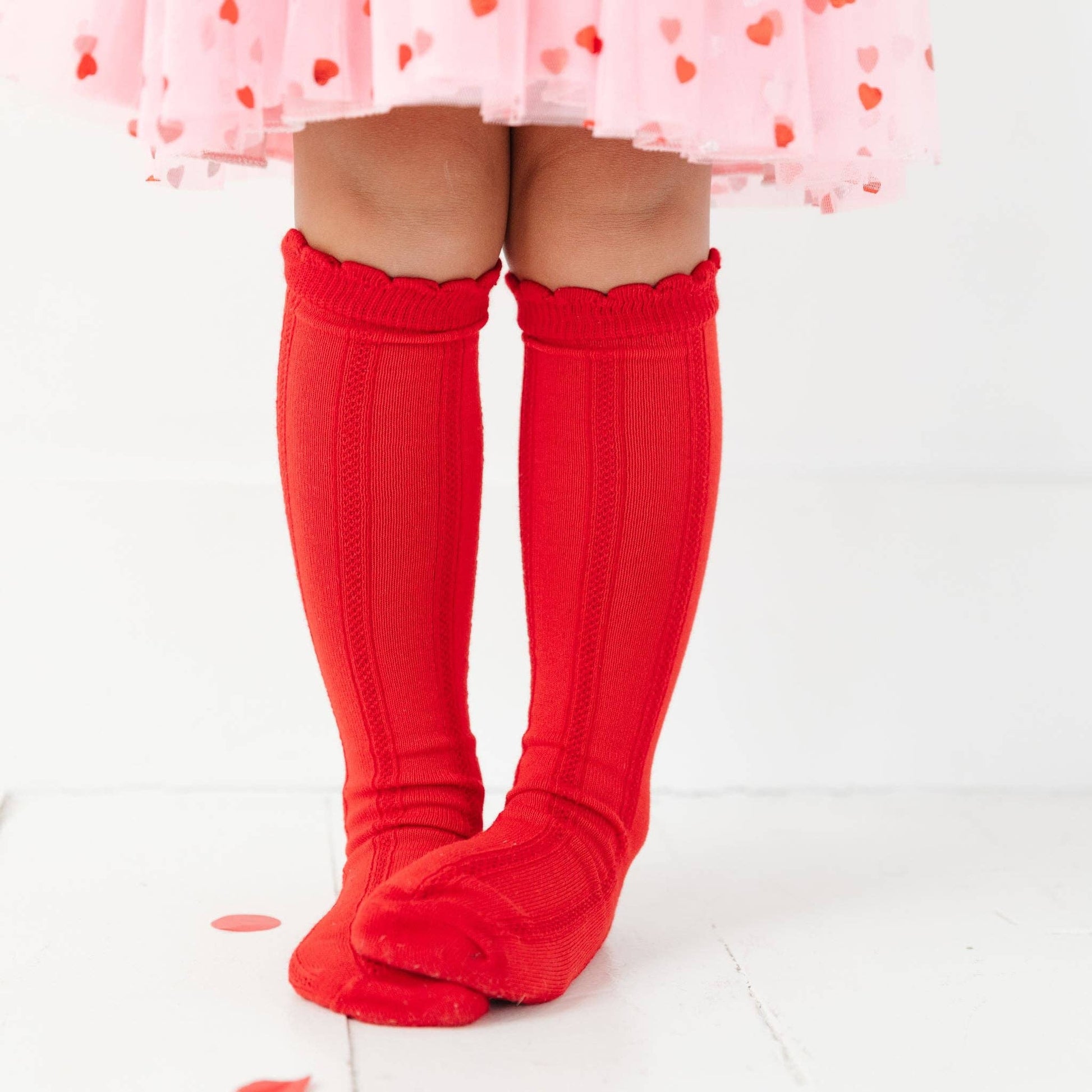 Red knee-high socks worn with a pink skirt on a white background
