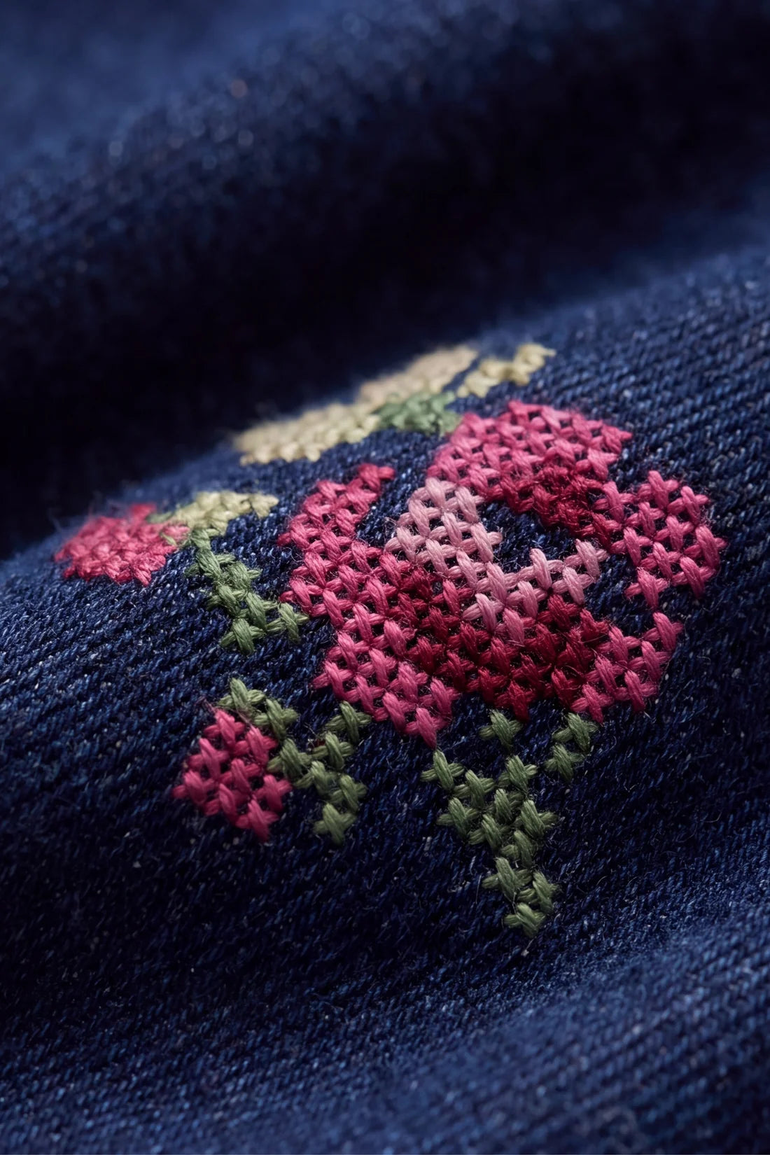 Close-up of a navy blue knit fabric featuring a colorful embroidered floral pattern with pink, red, and green stitches.