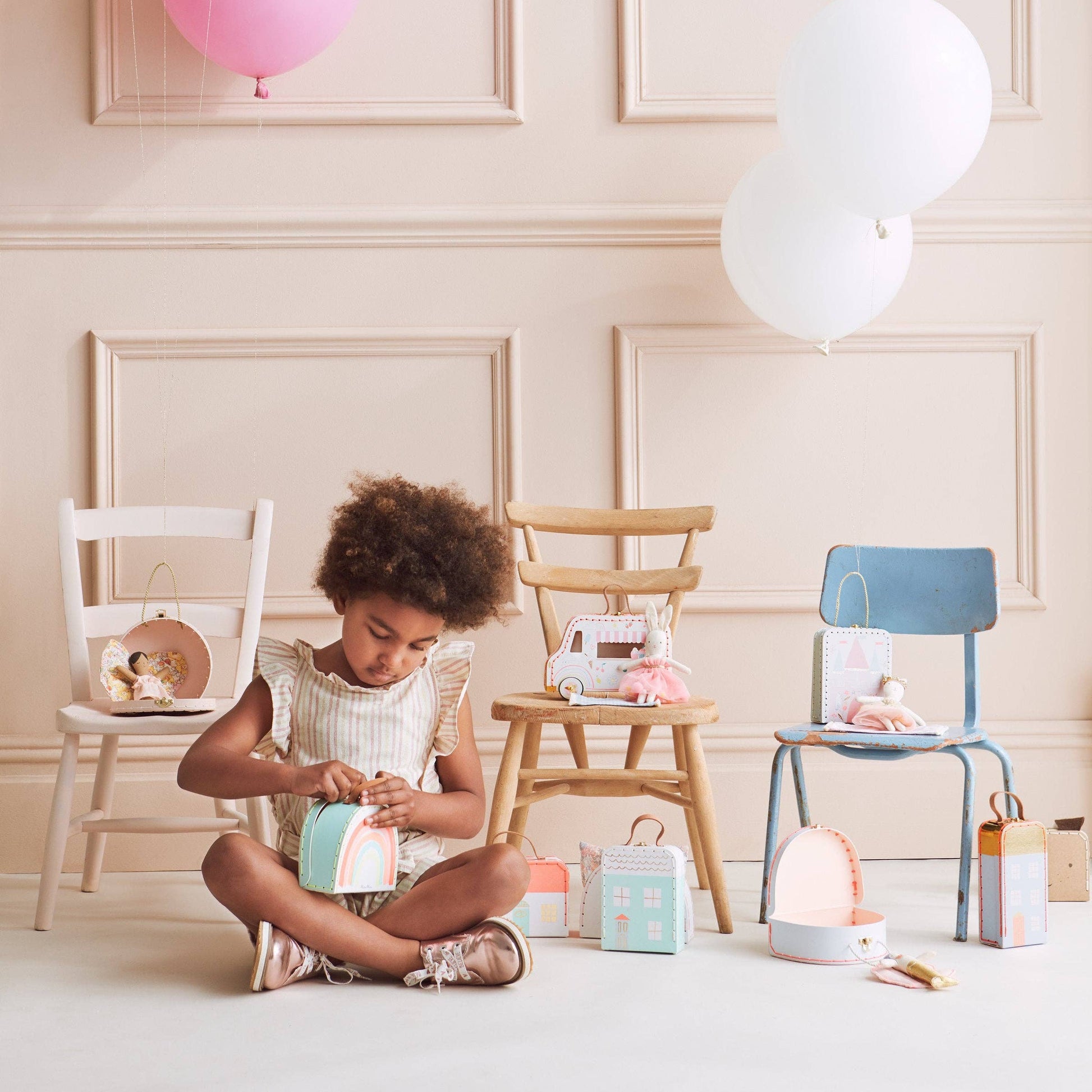 Child playing with colorful boxes in a room with wooden chairs and balloons.