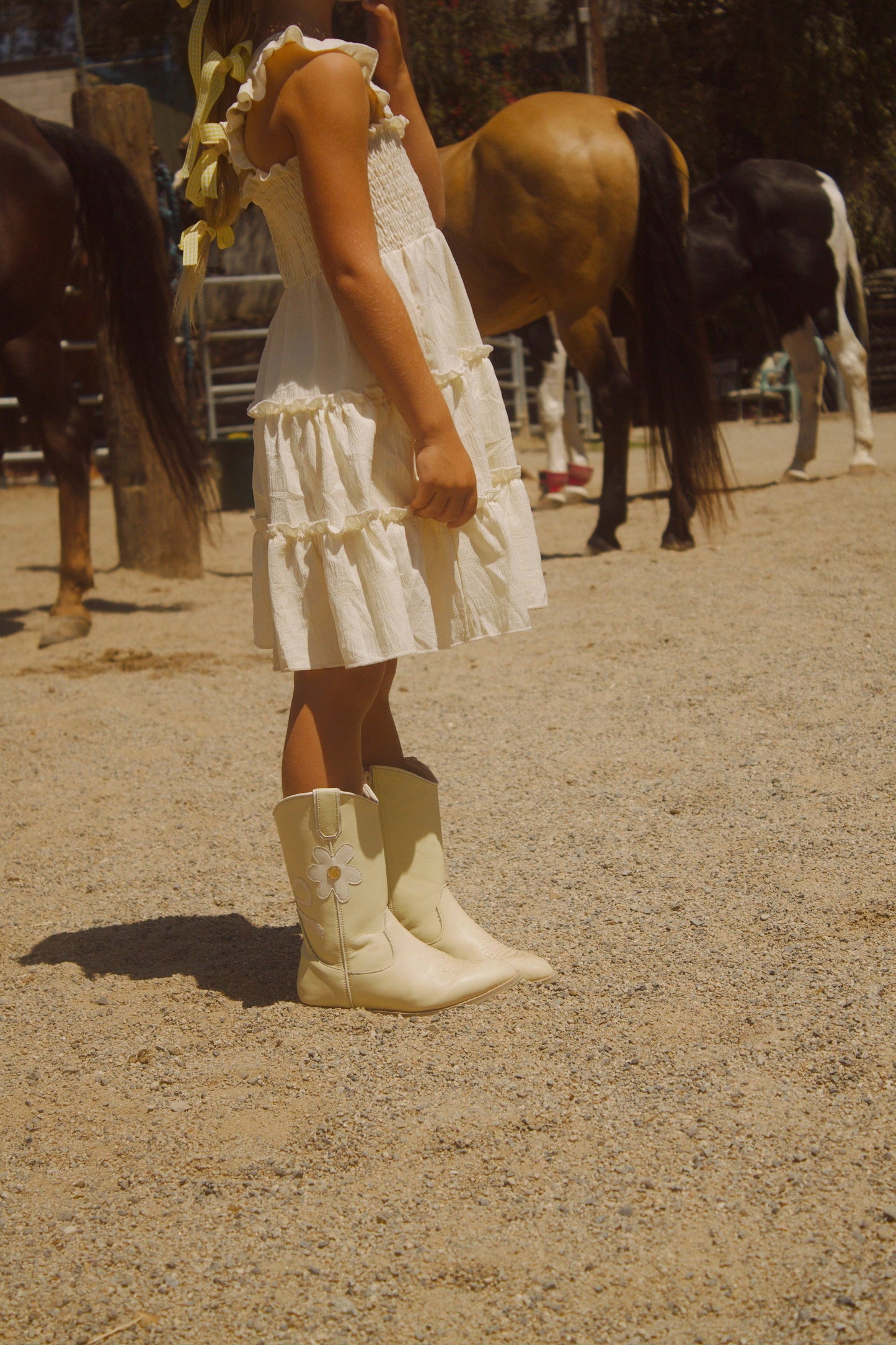 Person in a white dress and cowboy boots standing in front of horses in an outdoor setting
