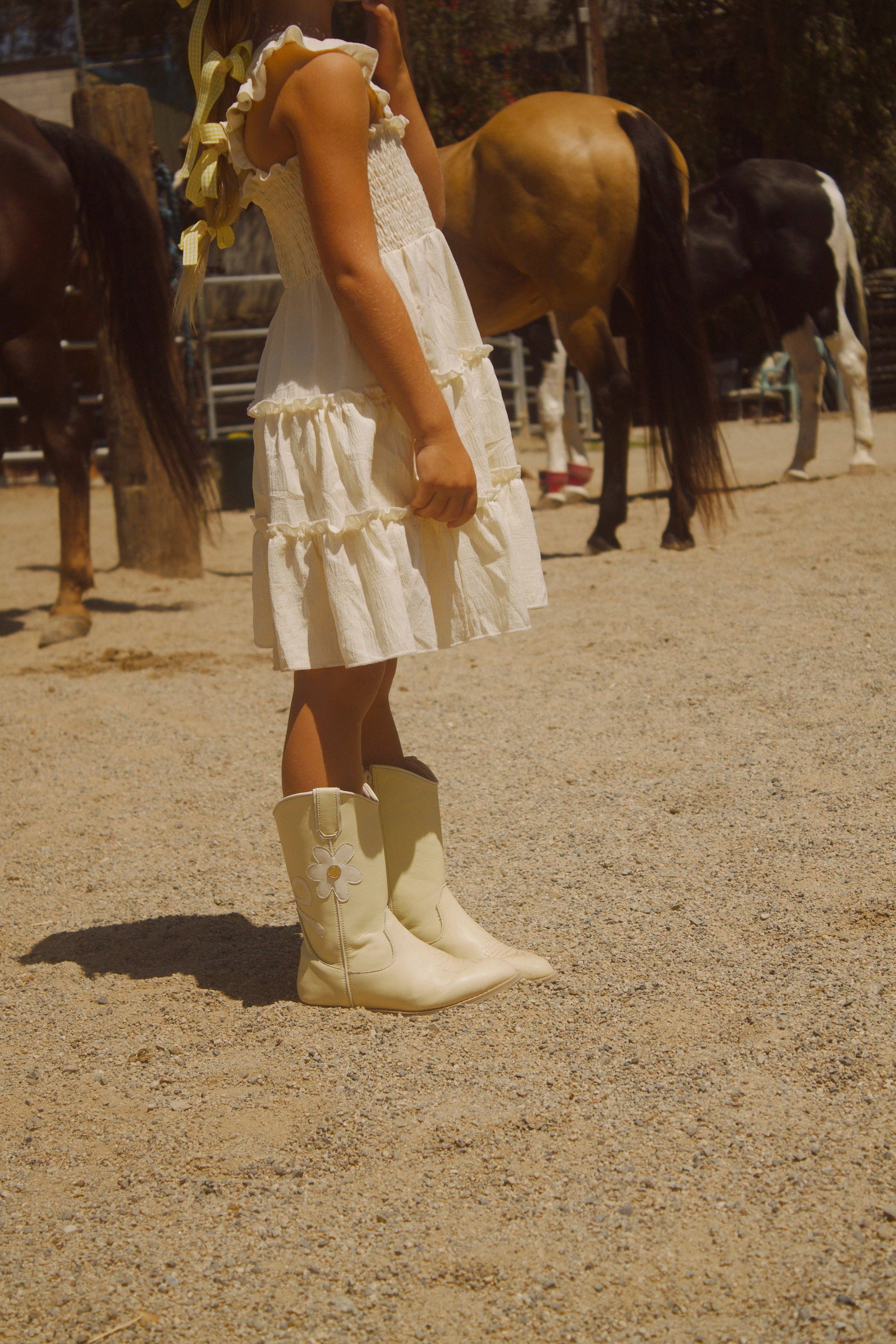 Person in a white dress and cowboy boots standing in front of horses in an outdoor setting