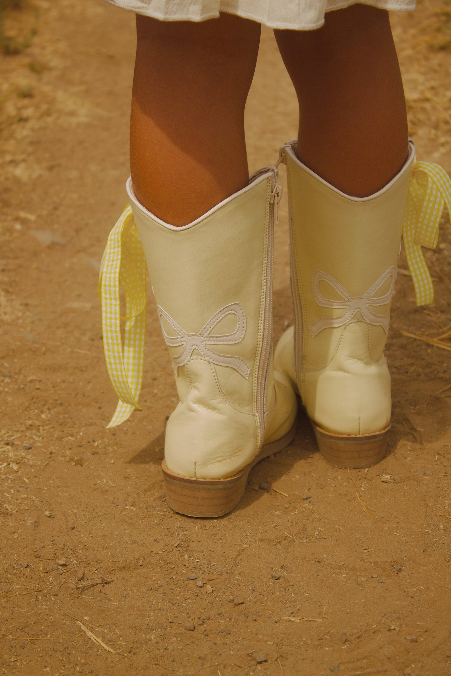 White cowboy boots with decorative bows on a dirt ground