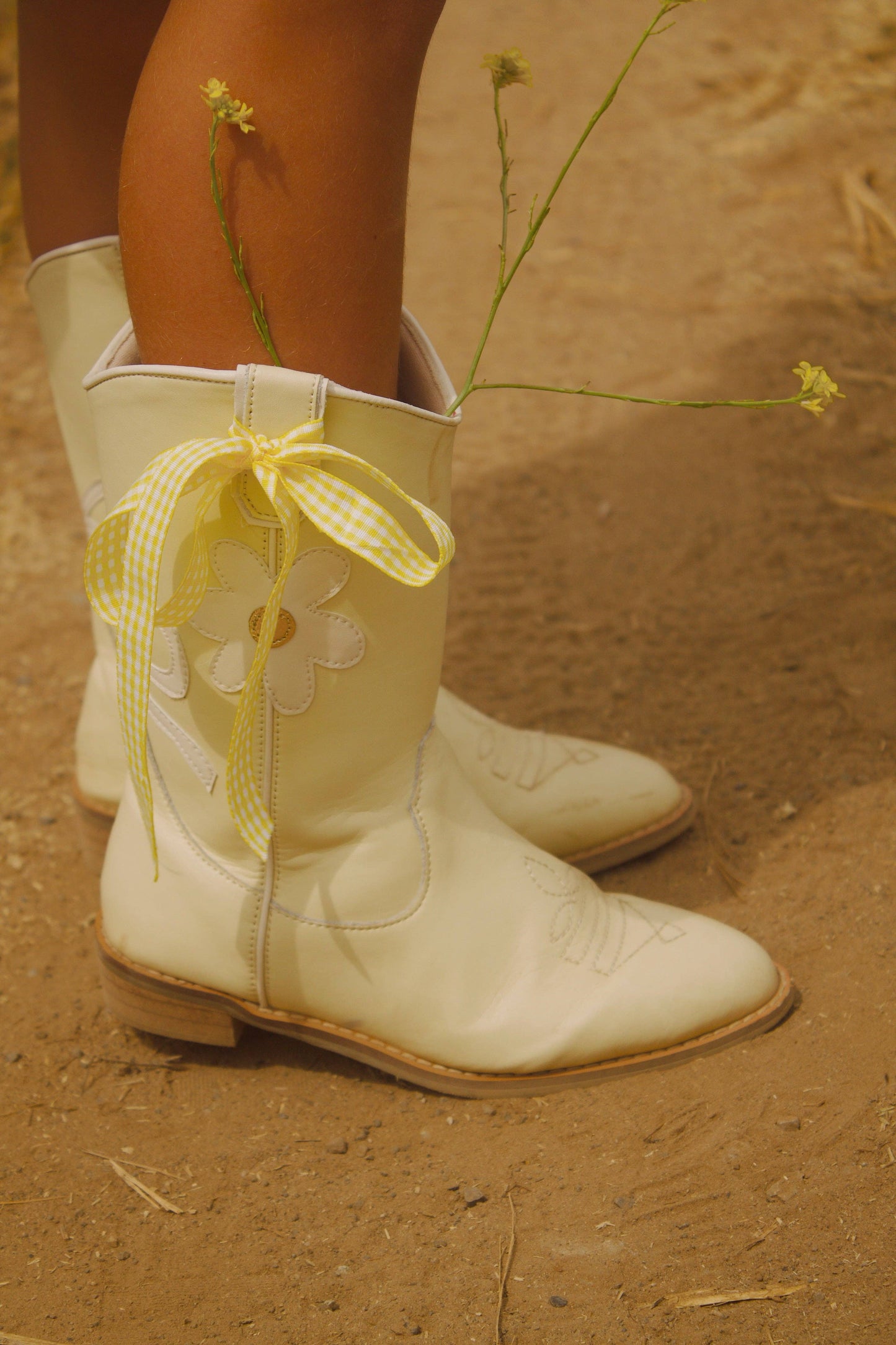 White cowboy boots with yellow ribbons on a dirt ground