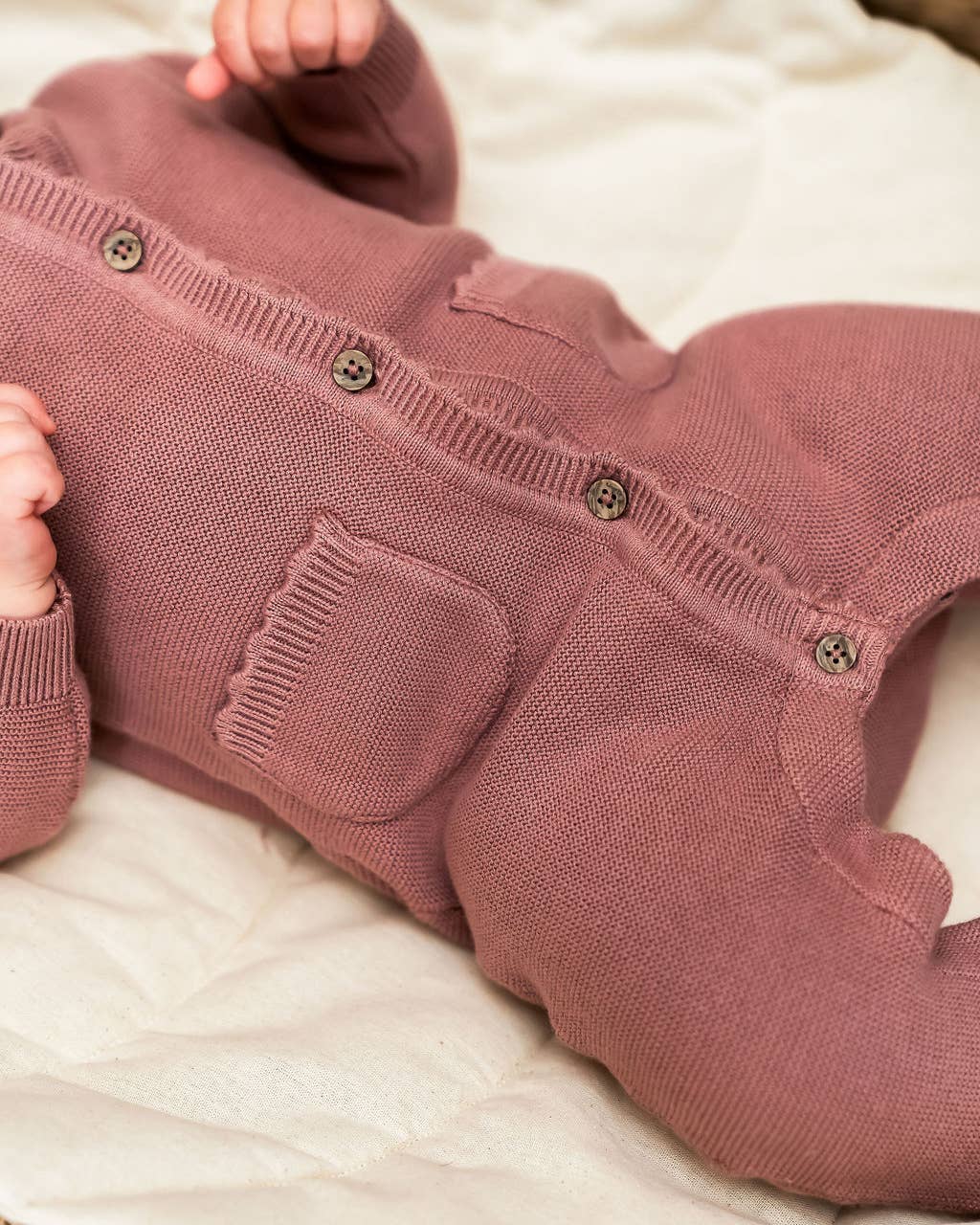 Close-up of a baby in a pink knitted outfit with buttons on a light background
