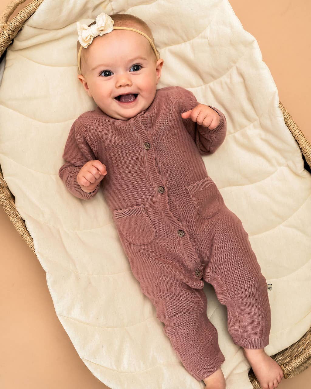 Baby in a pink onesie lying on a beige blanket