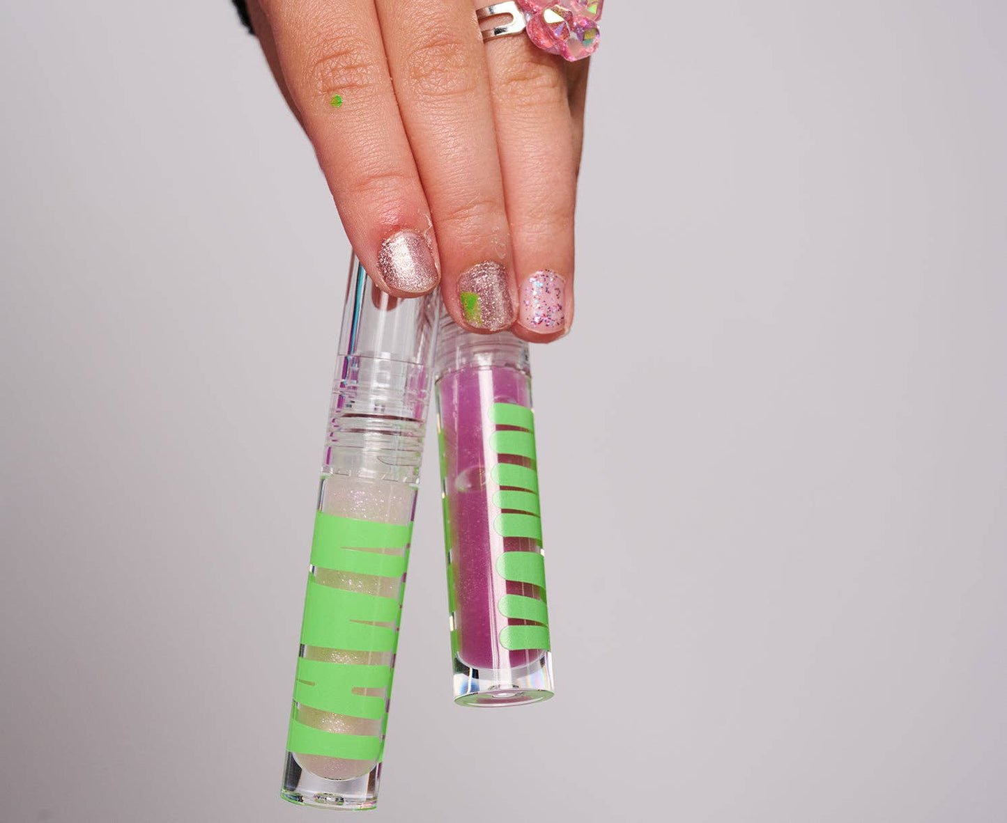 Hand holding two small cylindrical objects with green and pink striped designs against a gray background