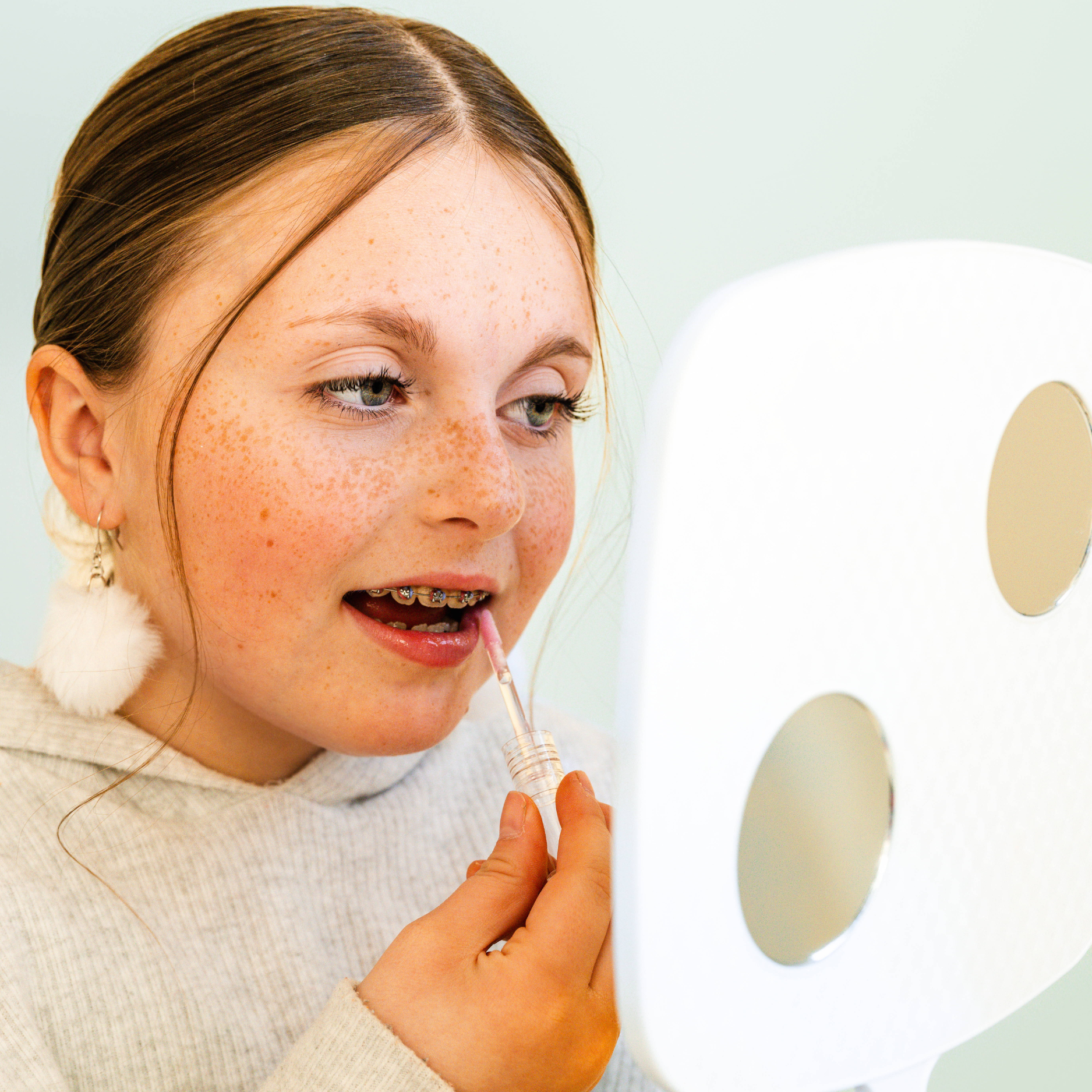 Person applying lip balm with a mirror reflection on a light background