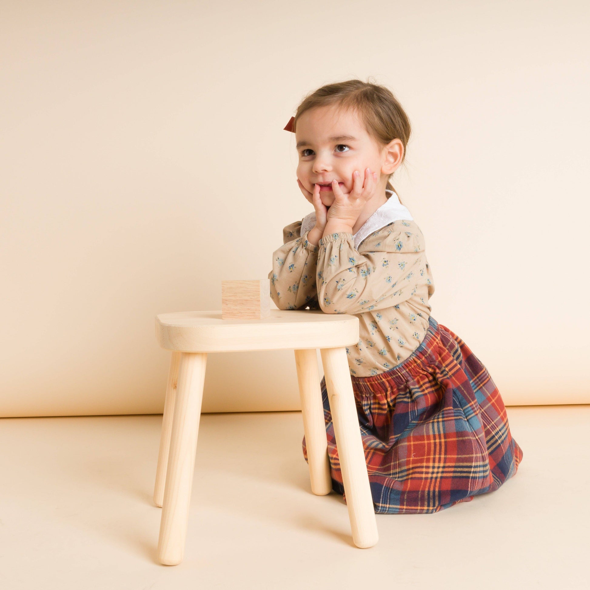 Young girl sitting on a small wooden stool with a neutral background