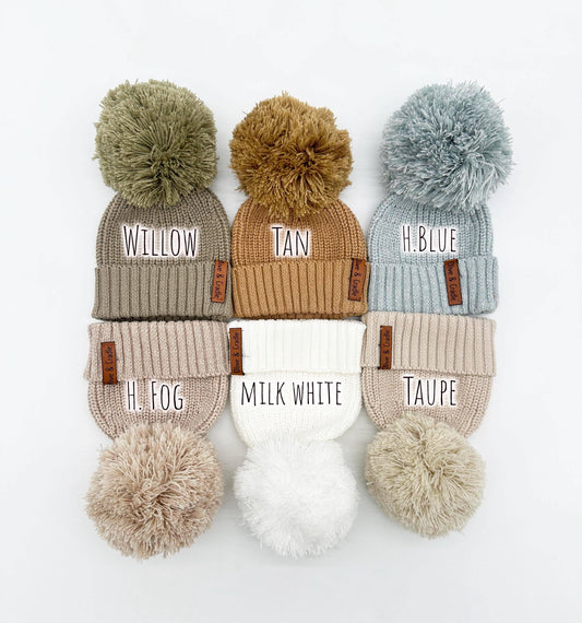 Set of six beanies with pom-poms in various colors on a white background