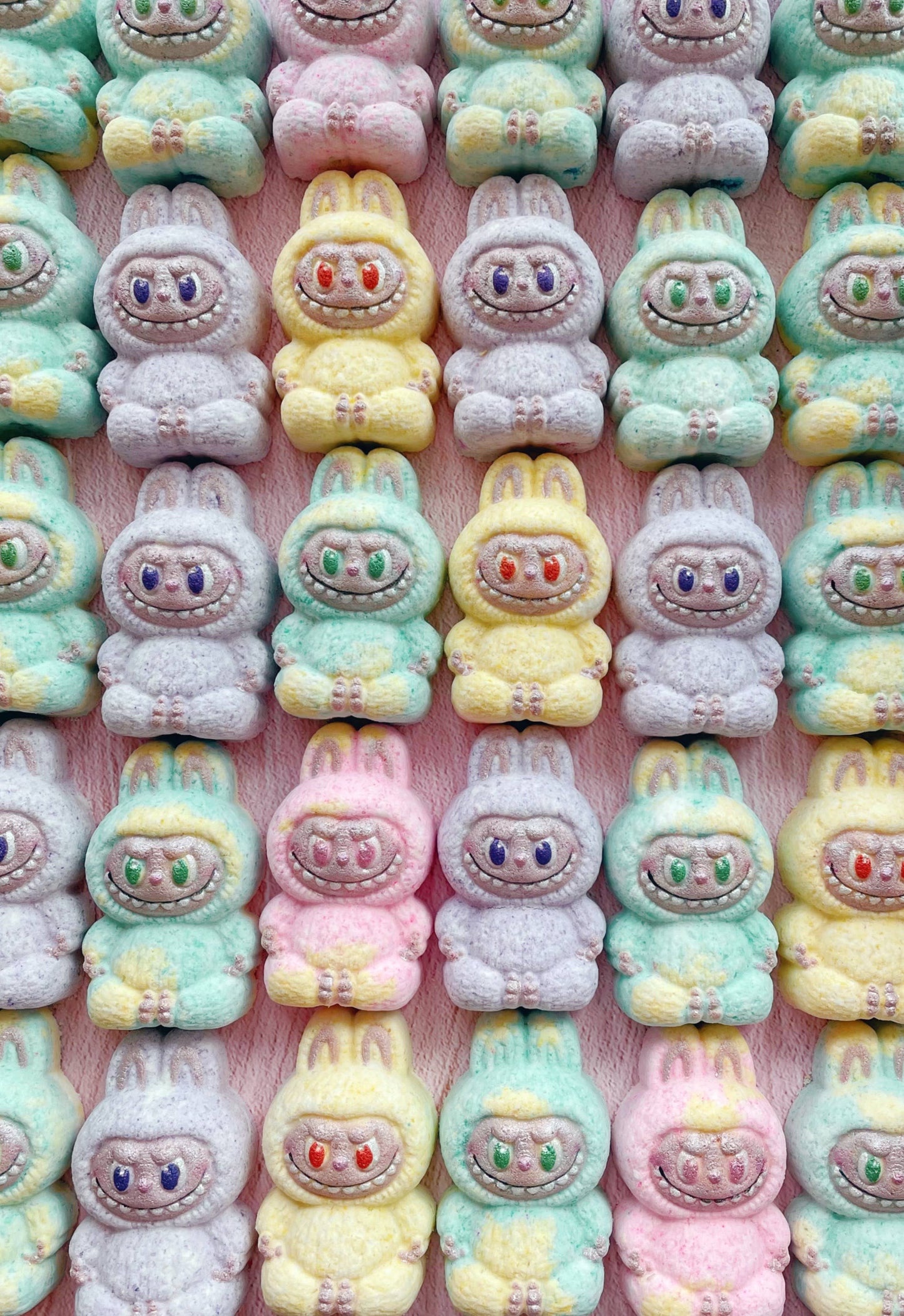 Pastel-colored cartoon character candies arranged in a grid on a pink background