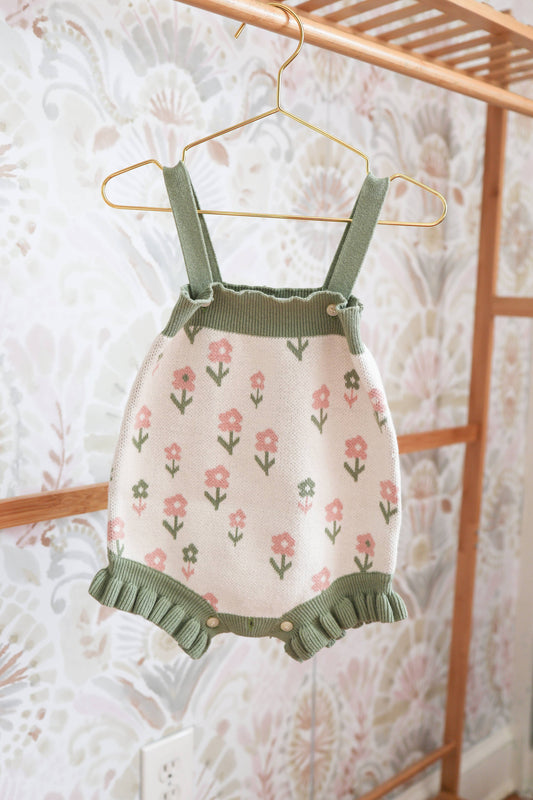 Children's floral dress with green straps and ruffles hanging on a rack.