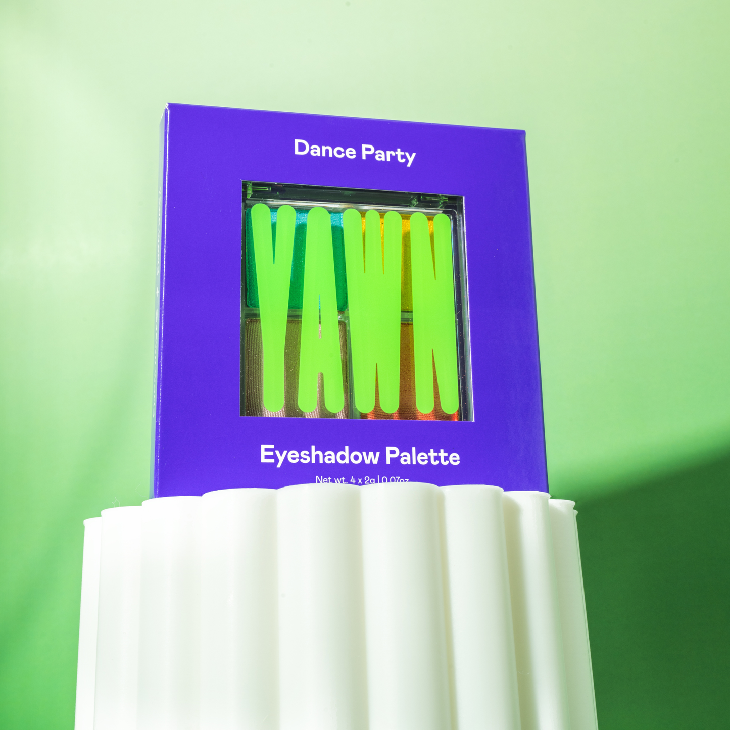 Eyeshadow palette with green shades on a purple box against a green background