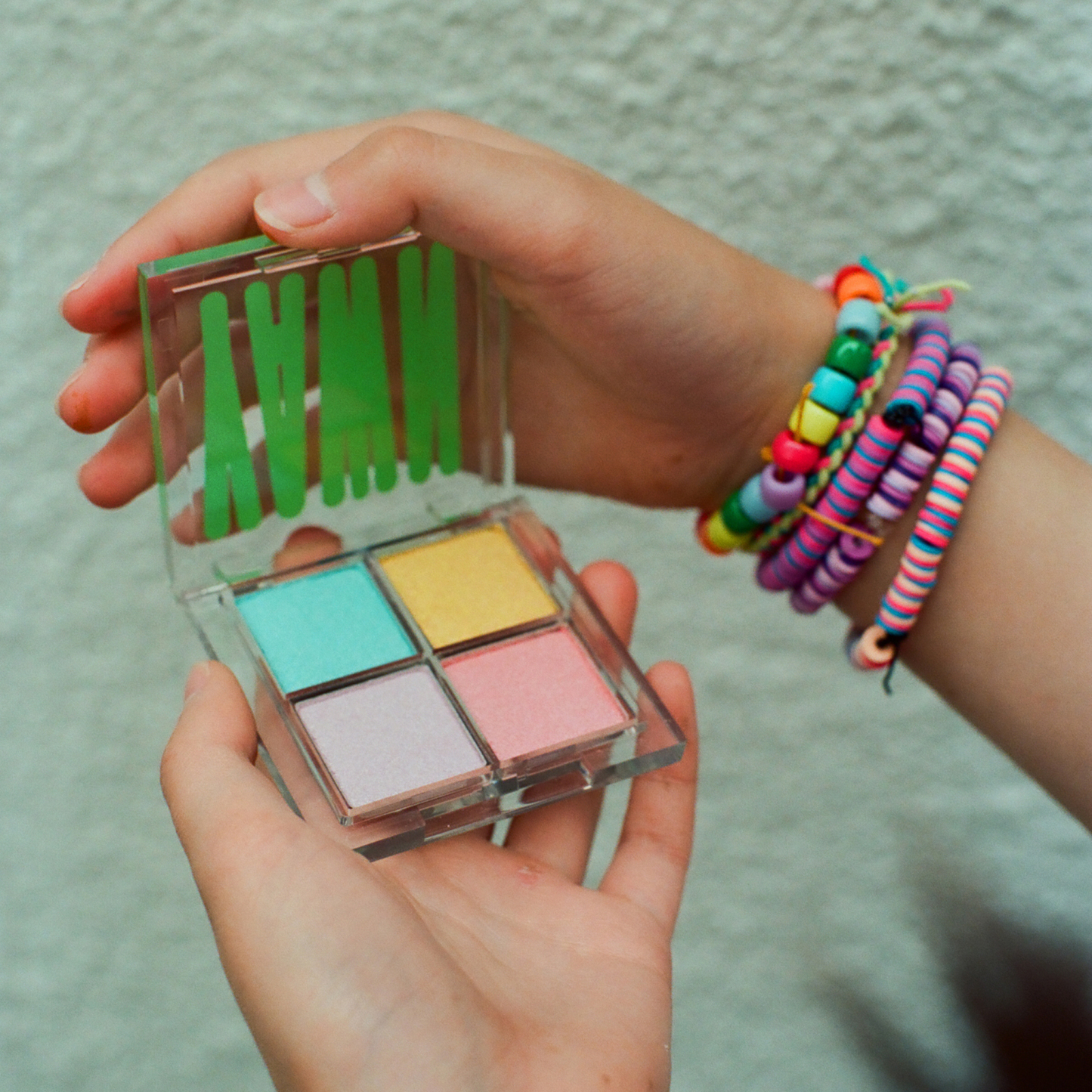 Hand holding a small makeup palette with colorful shades against a textured background