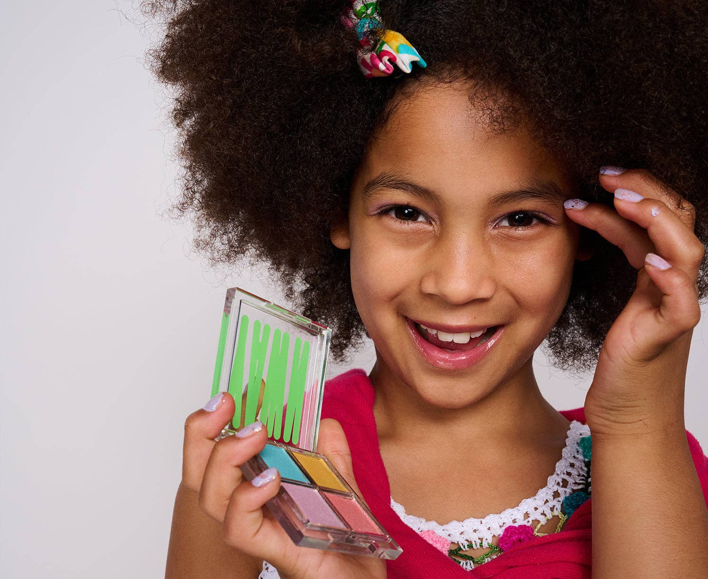 Young girl holding a small mirror with colorful reflection against a plain background
