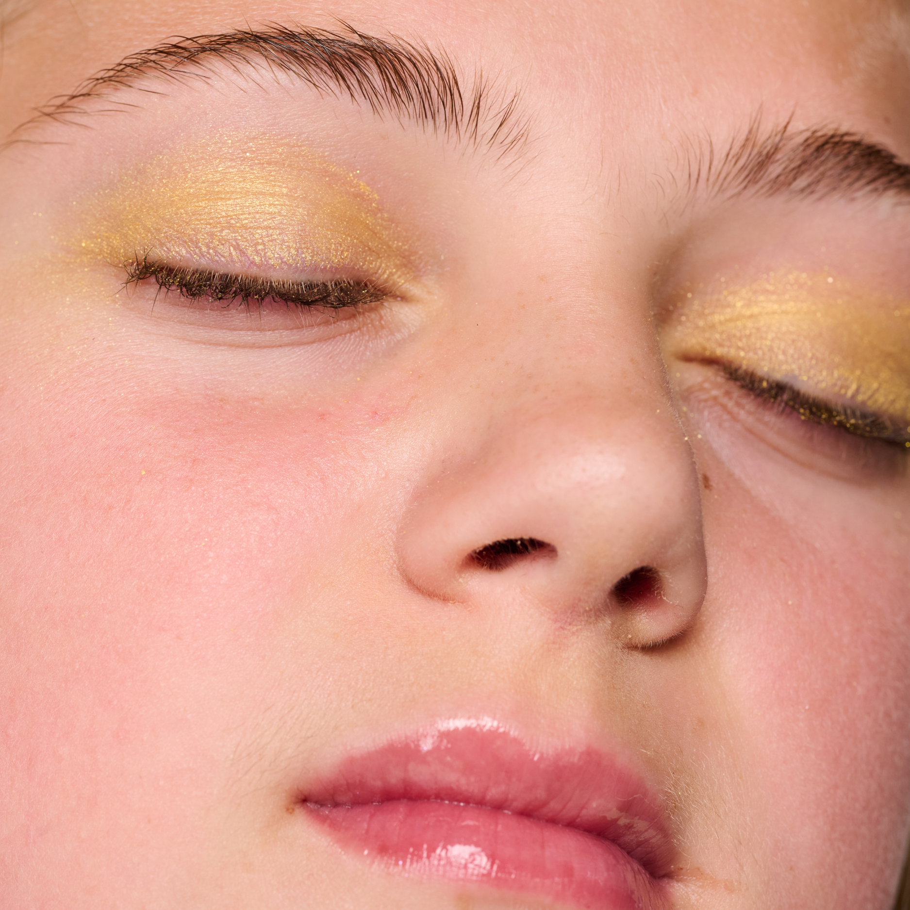 Close-up of a person with gold eye makeup and pink lips.