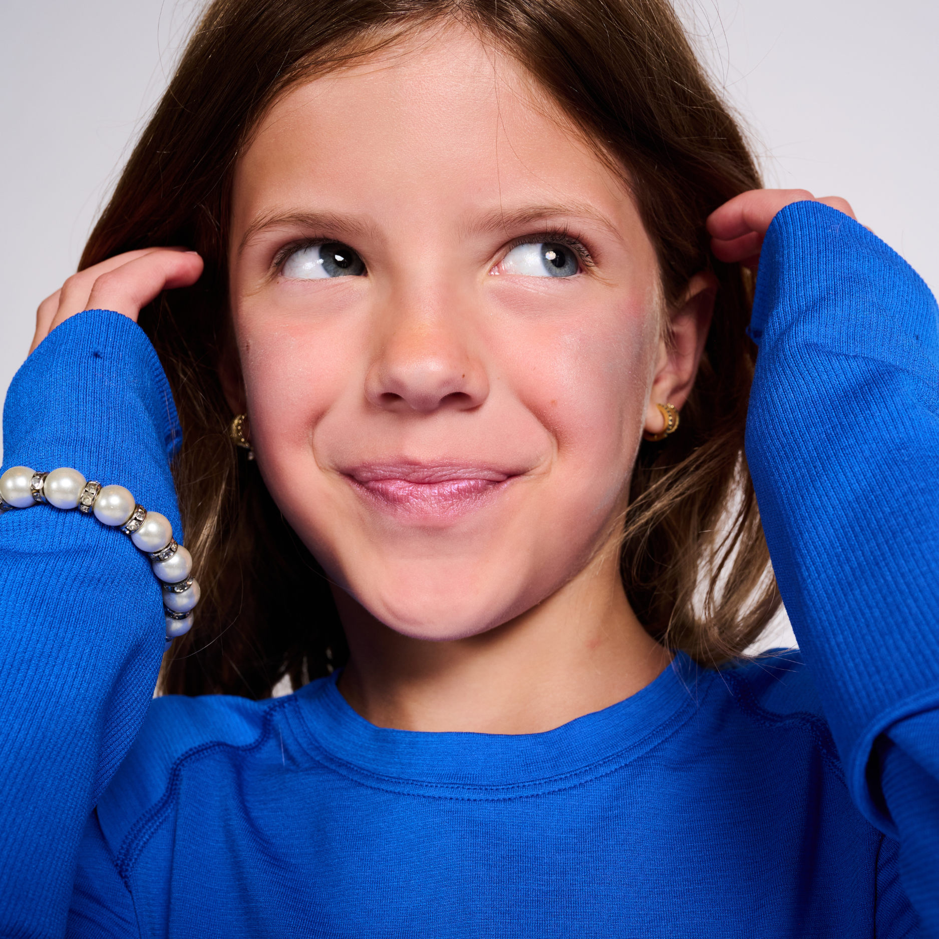 Young girl wearing a blue sweater with pearl bracelet on a plain background