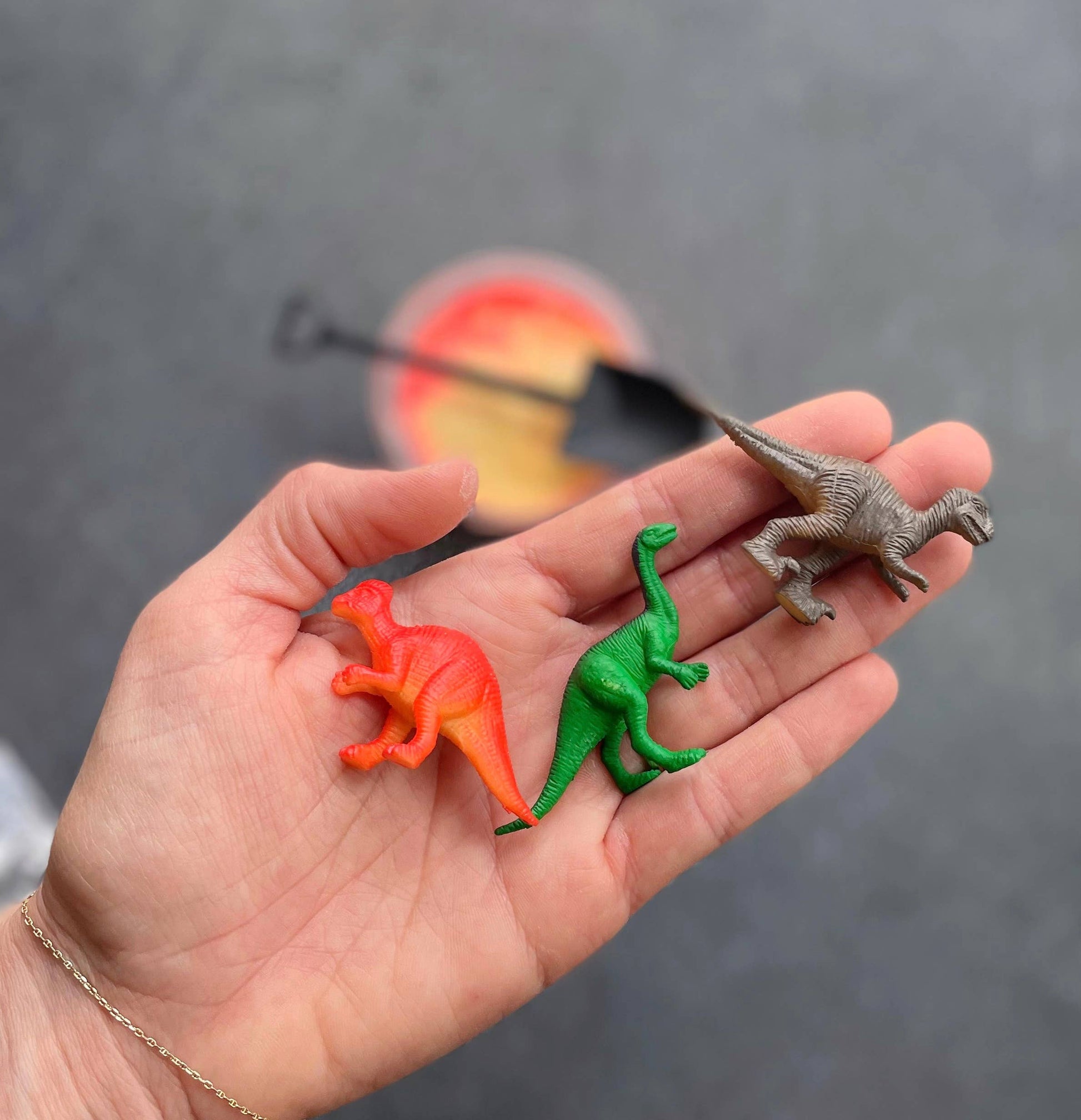 Hand holding three toy dinosaurs in front of a blurred background