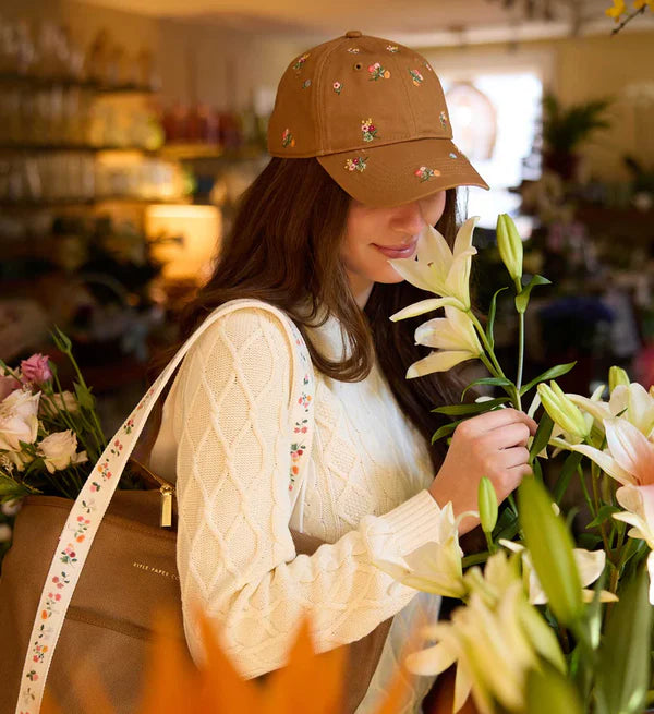 Woman holding flowers in a floral shop wearing a brown cap with floral patterns.