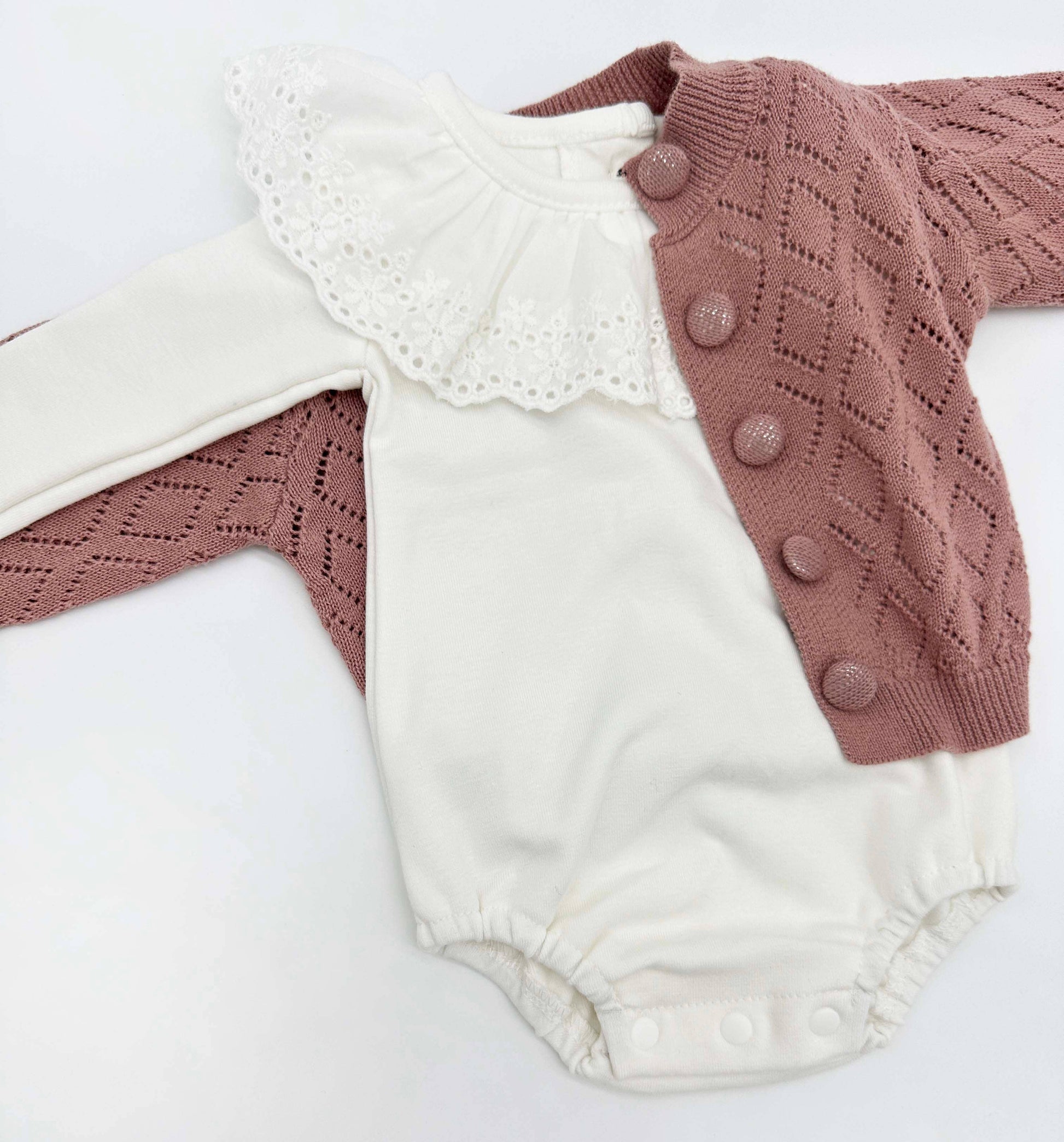 White baby romper with pink cardigan on a white background