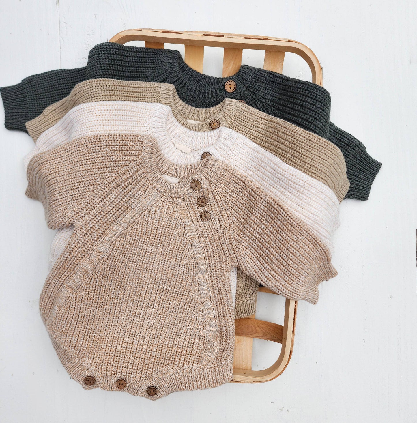 Knitted baby rompers in various colors on a wooden chair against a white background