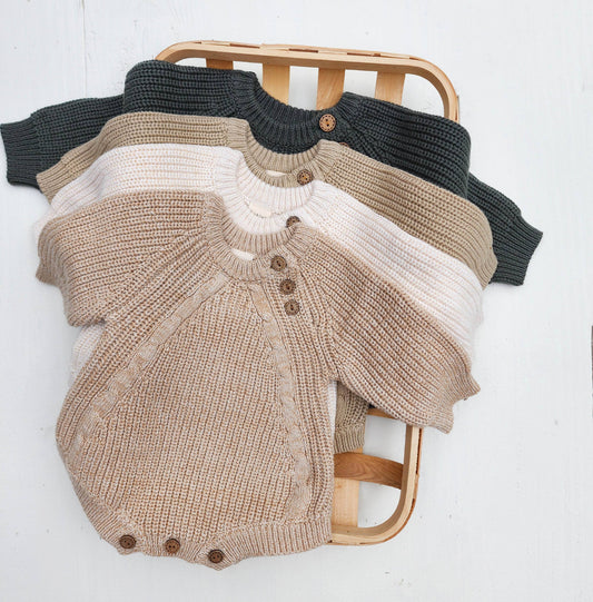 Knitted baby rompers in various colors on a wooden chair against a white background