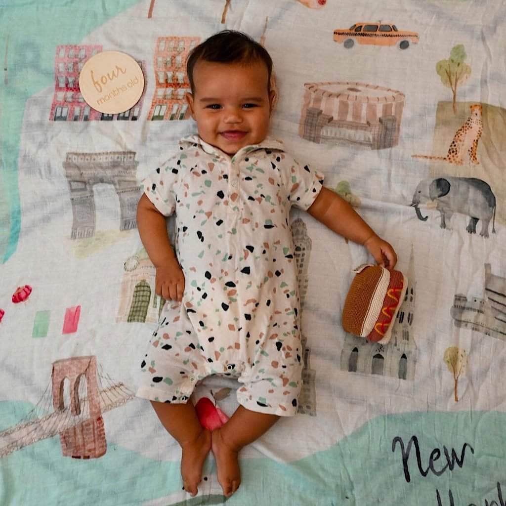 Baby in a patterned outfit sitting on a colorful quilt with toys.