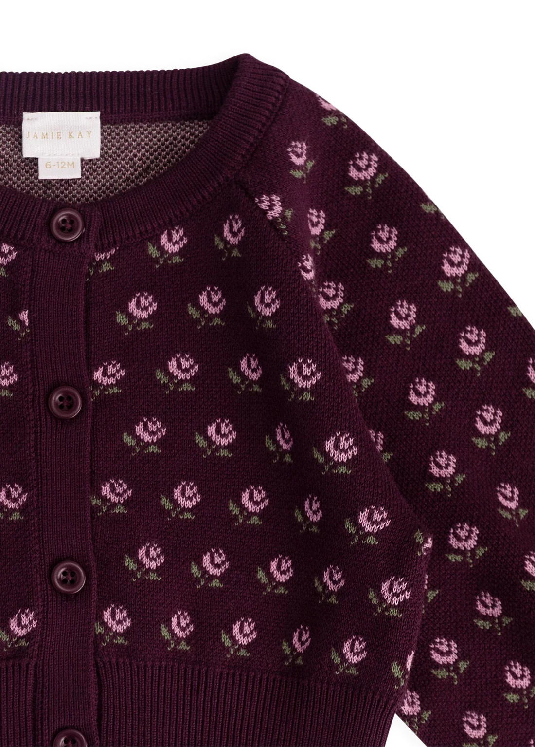 A close-up of a knit cardigan sweater in deep plum purple, featuring a repeating pattern of small pink flowers with green leaves. The cardigan has dark brown buttons and a ribbed collar, cuffs, and hem.