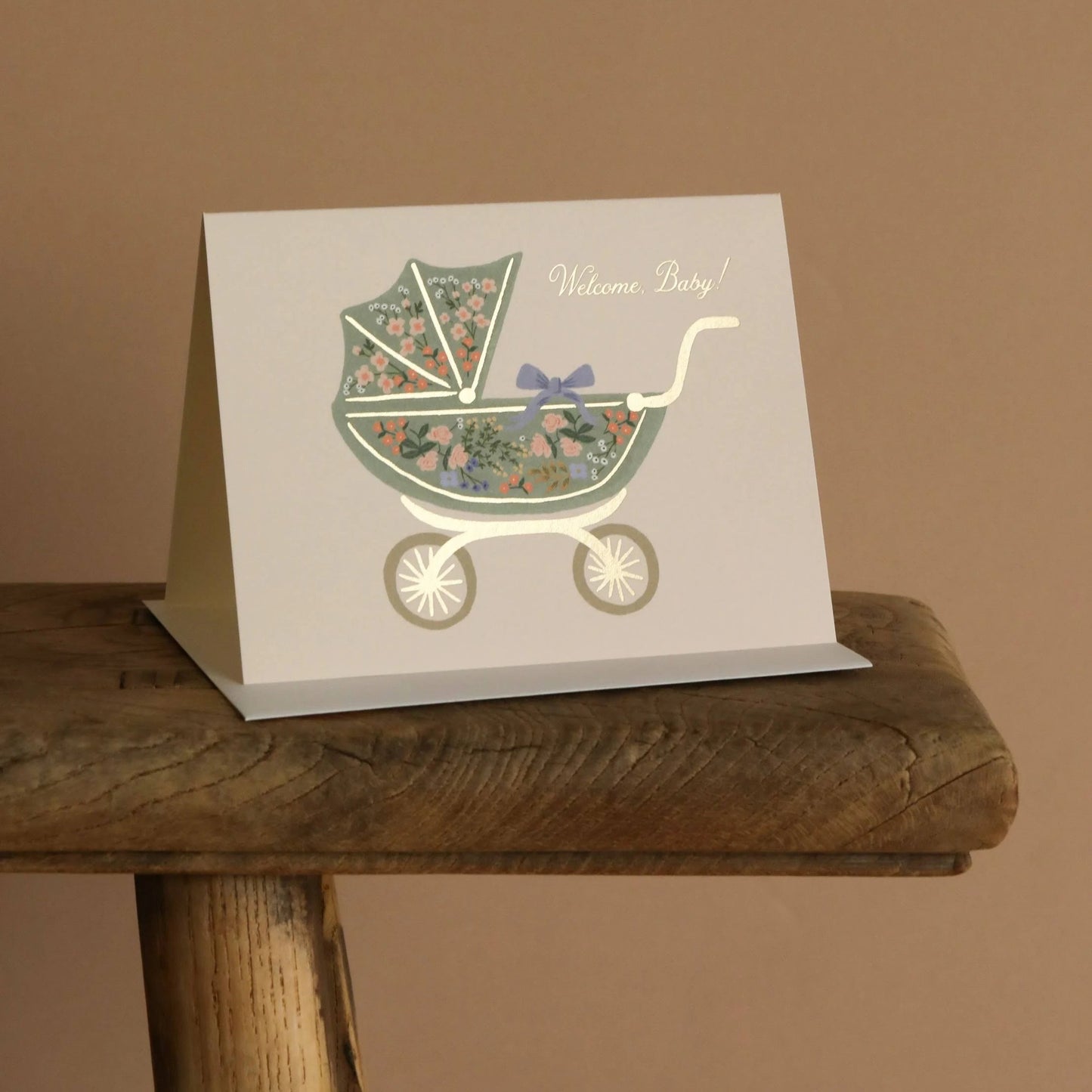 Greeting card with floral baby buggy design on a wooden surface against a brown background