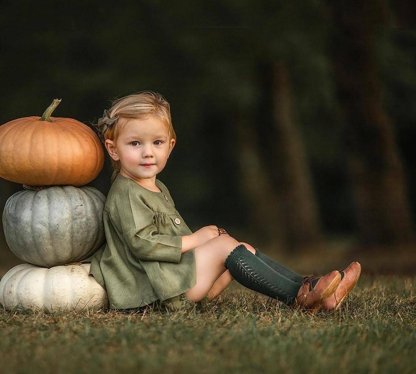Child sitting on the grass with pumpkins in a natural setting