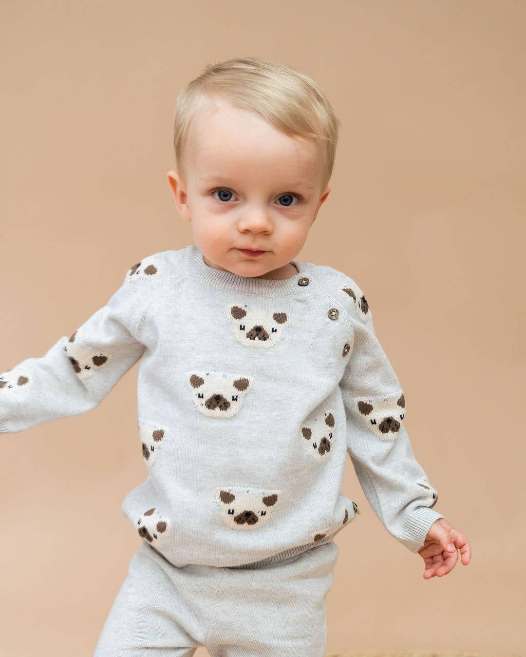 Child wearing a light gray sweater with bear patterns on a beige background