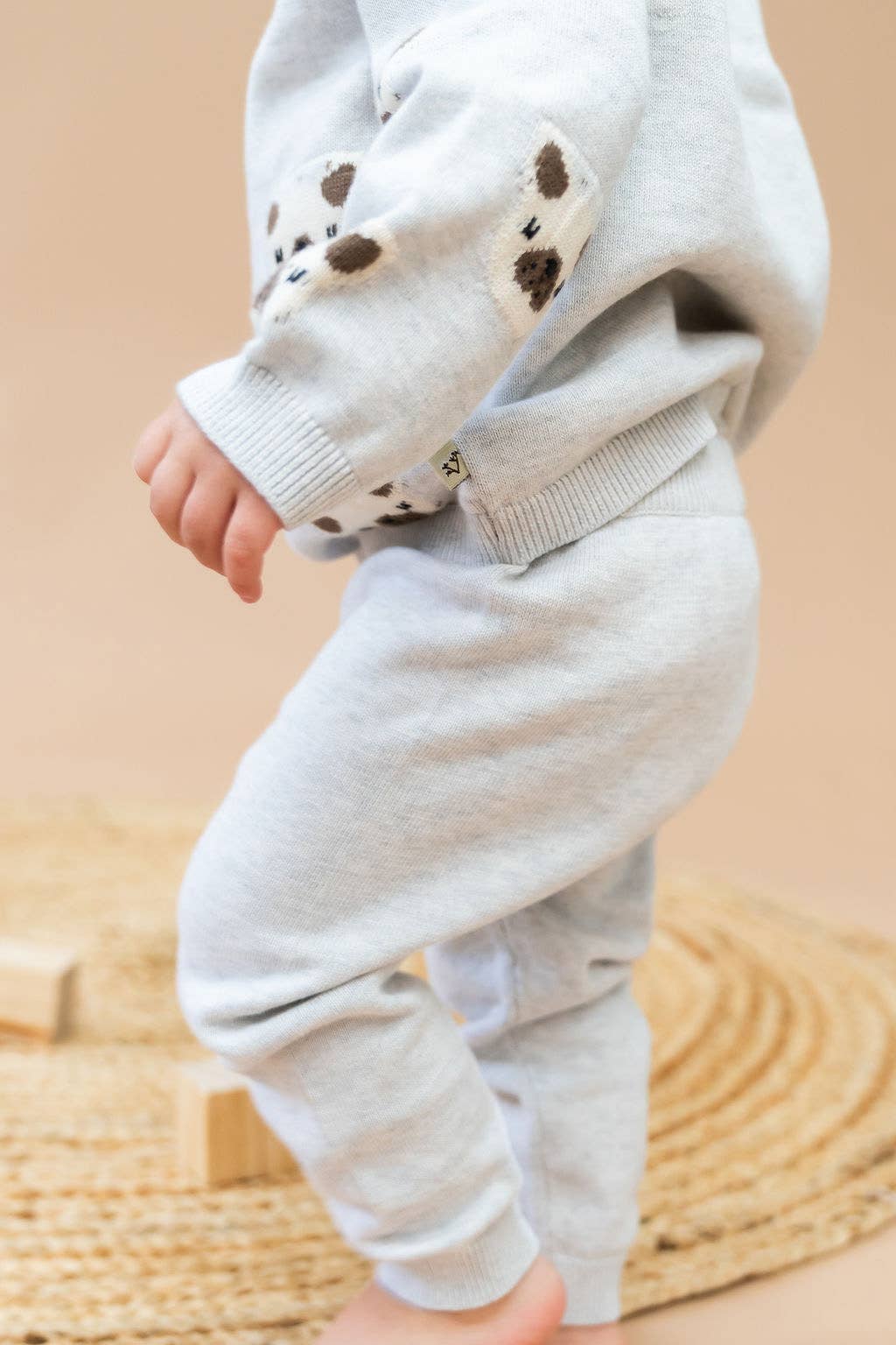Child wearing a light gray outfit with paw print details on a beige background