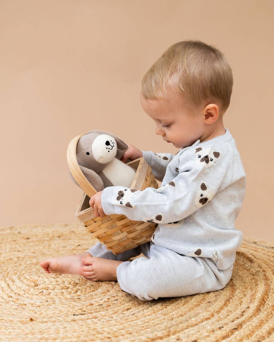 Child playing with a plush toy in a basket on a woven mat