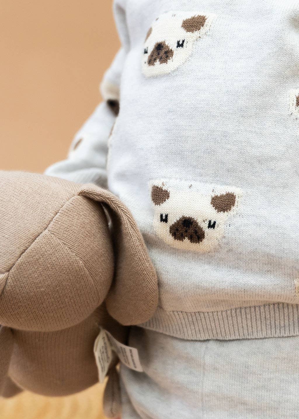 Close-up of a child wearing a light gray hoodie with bear face patches on a beige background