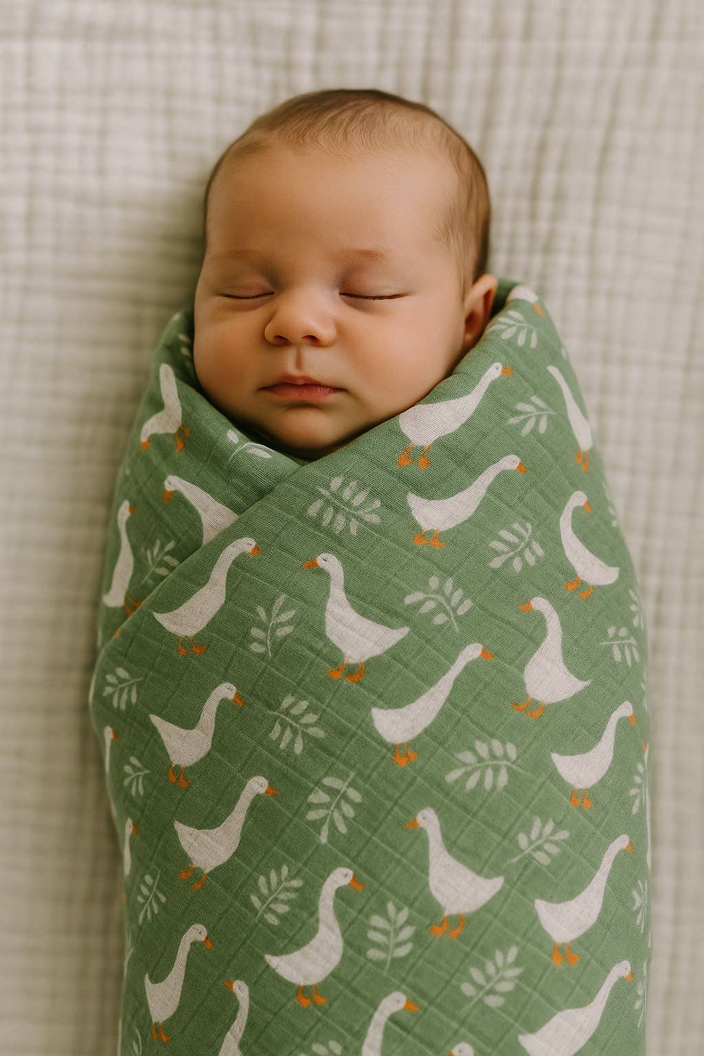 Newborn baby swaddled in a green blanket with goose pattern on a textured surface