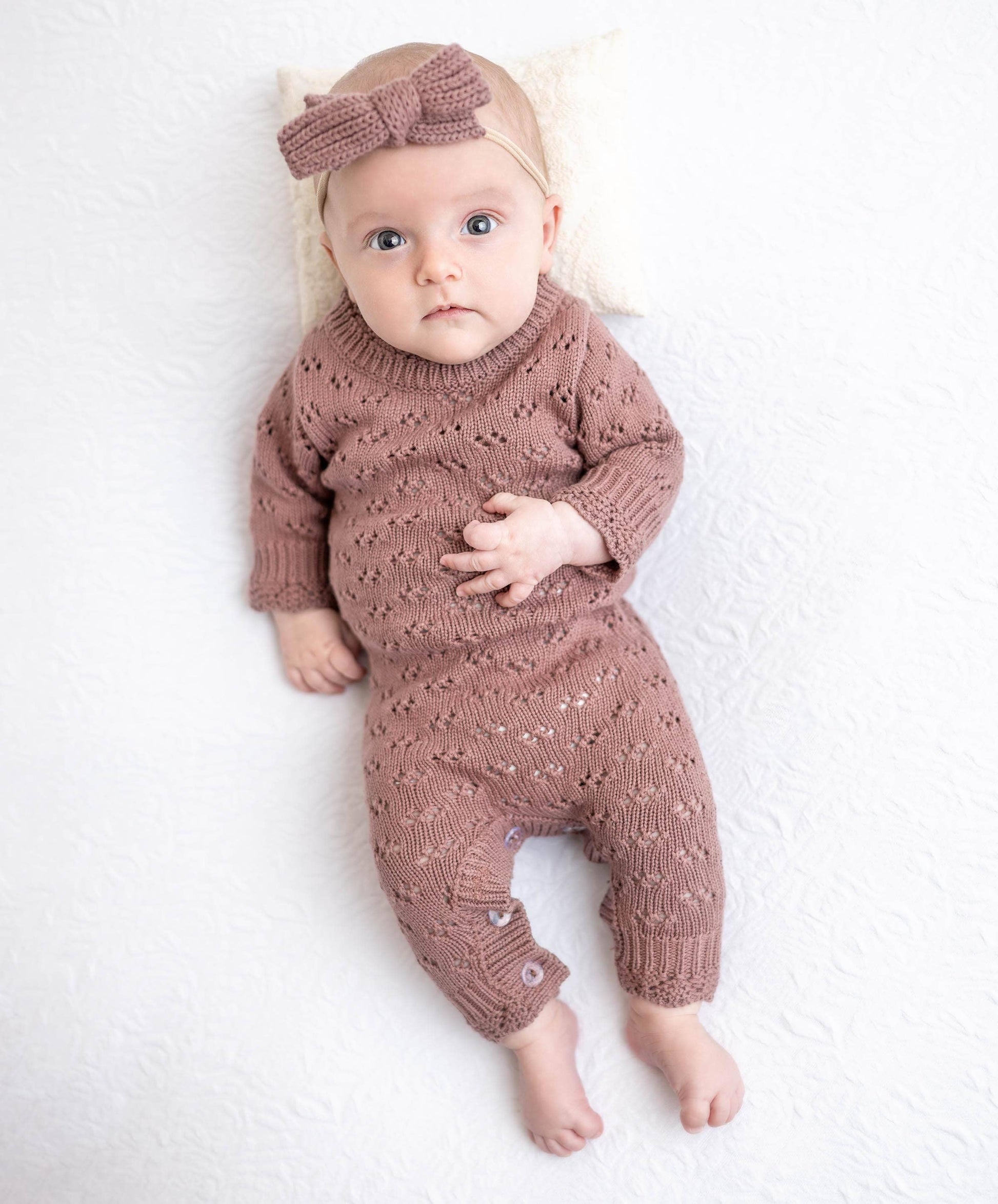 Baby wearing a knitted brown outfit with a matching headband on a white background