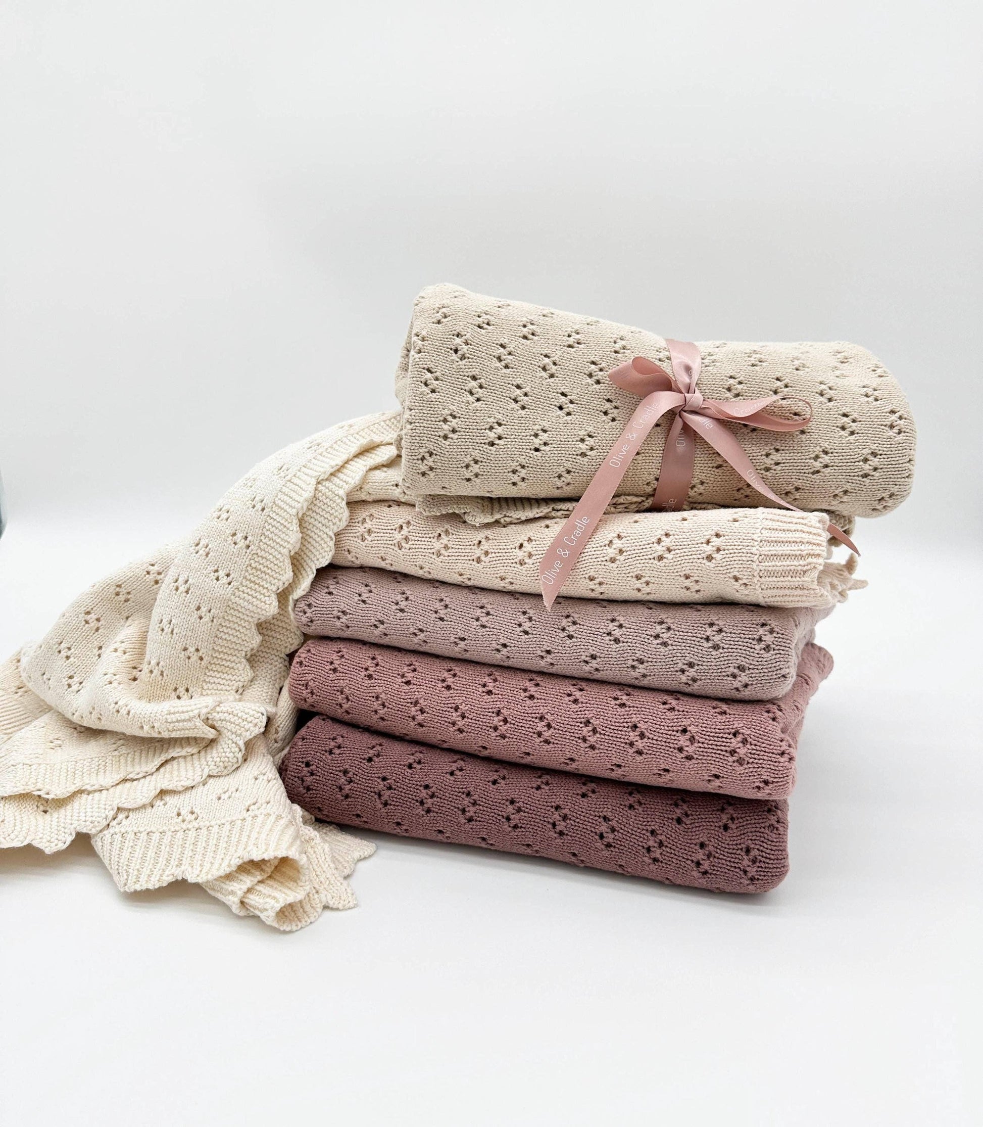 Stack of folded baby blankets in various shades of pink and cream on a white background