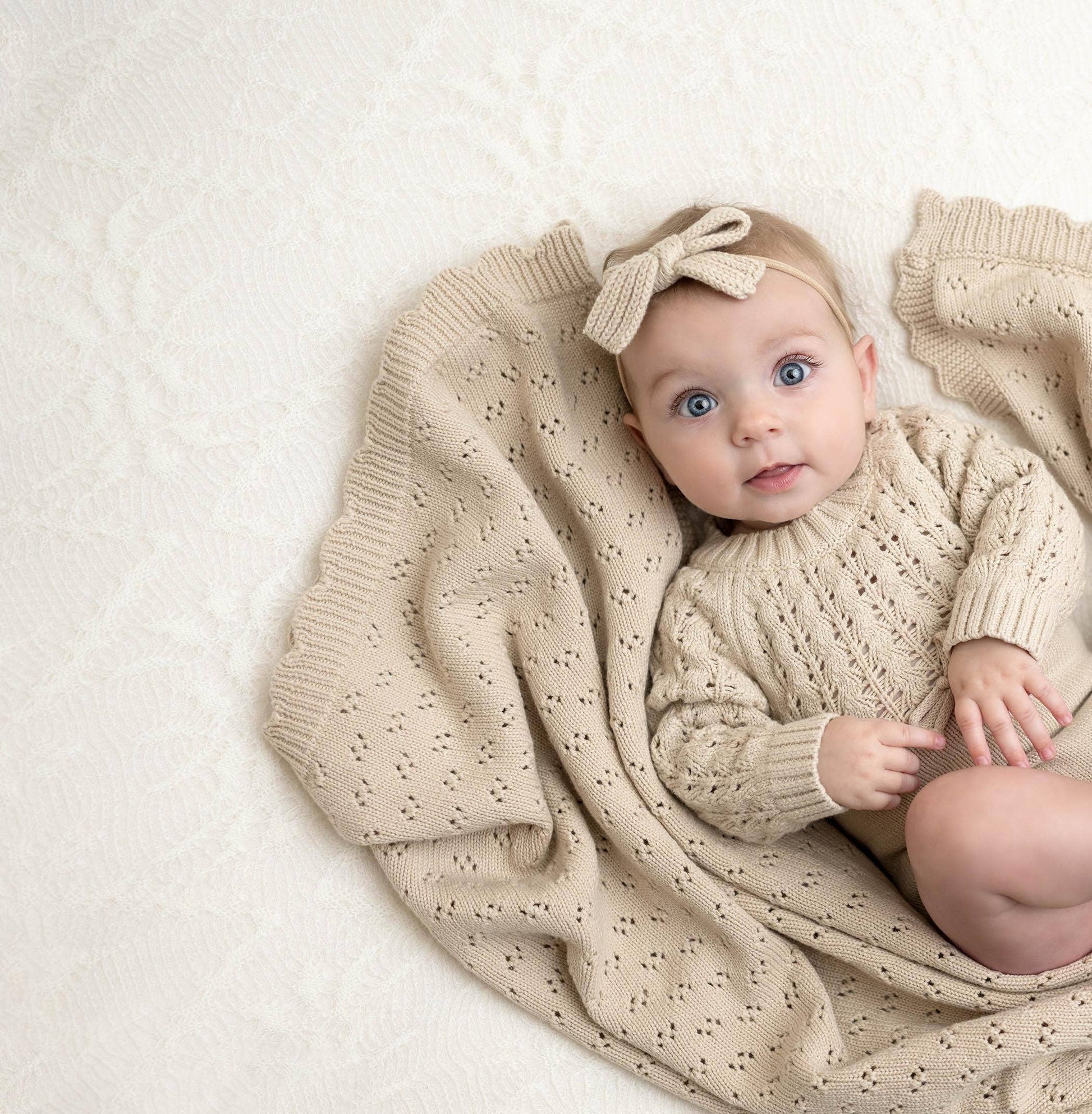 Baby wrapped in a beige knitted blanket with a matching headband on a light background