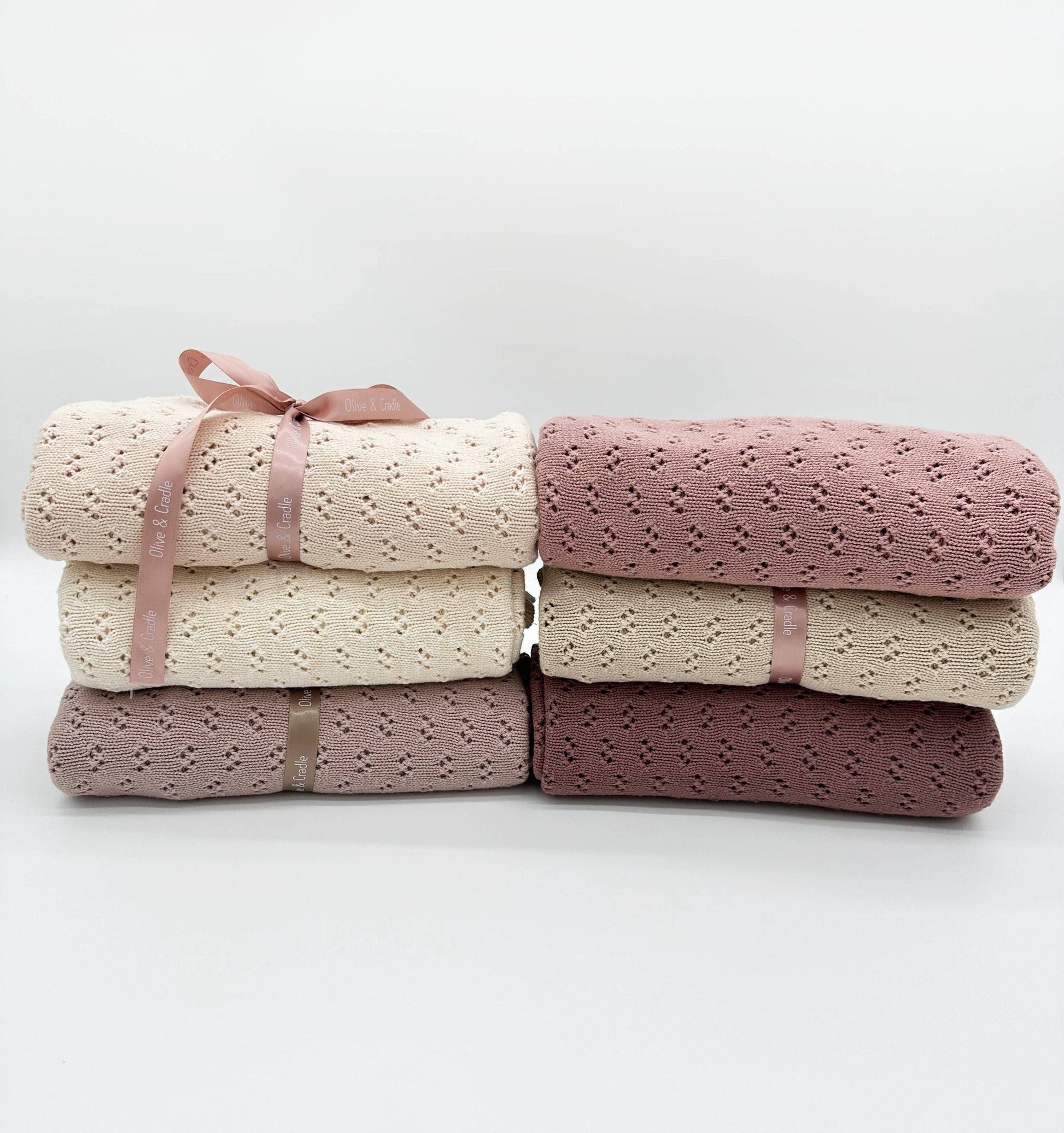 Stack of folded blankets in pink and beige with ribbons on a white background