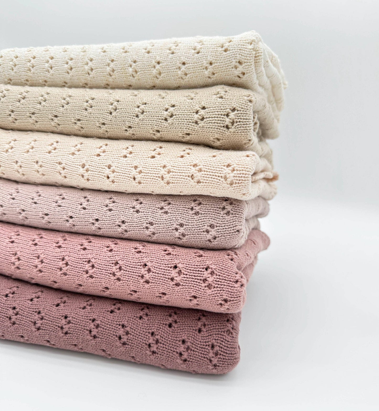 Stack of folded knit blankets in beige, pink, and rose on a light gray background