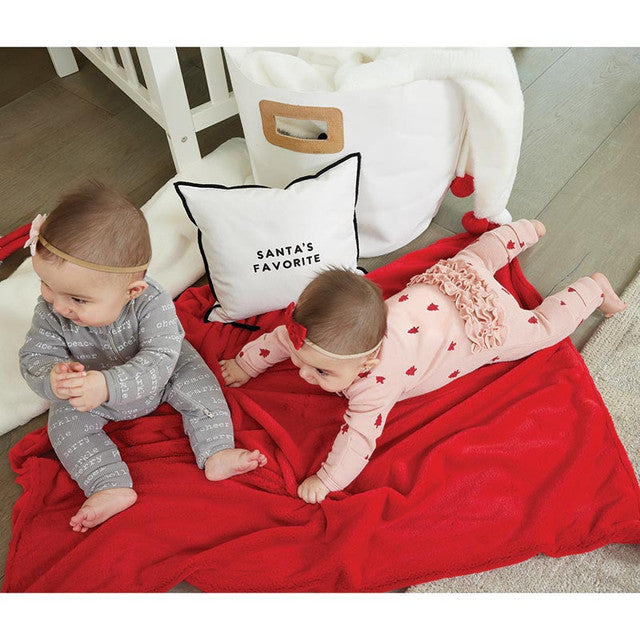 Two babies on a red blanket with a 'Santa's Favorite' pillow in the background