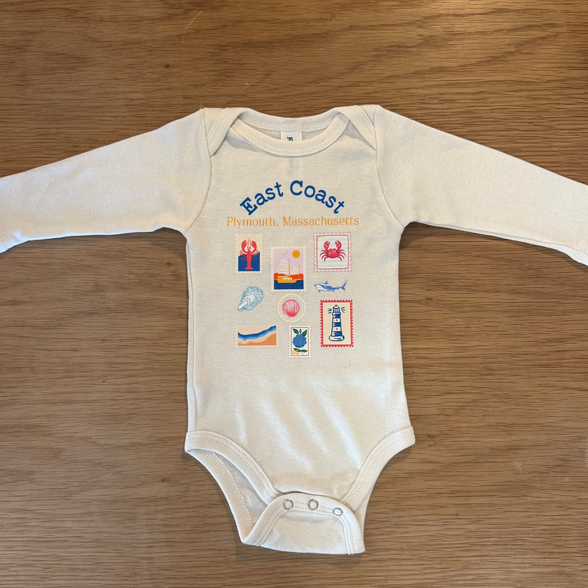 Ivory onesie with East Coast Plymouth Massachusetts printed on it. Nautical prints on the shirt as well such as lobsters, sharks, oysters, seashells, sail boats, the beach, and hydrangeas. 