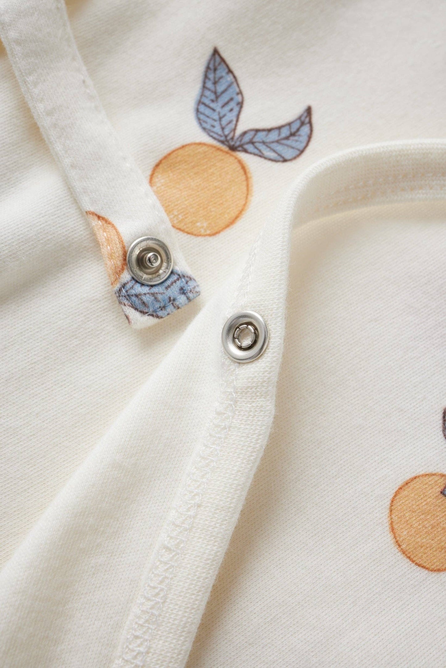 Close-up of a white fabric with orange and blue leaf patterns and metal buttons.