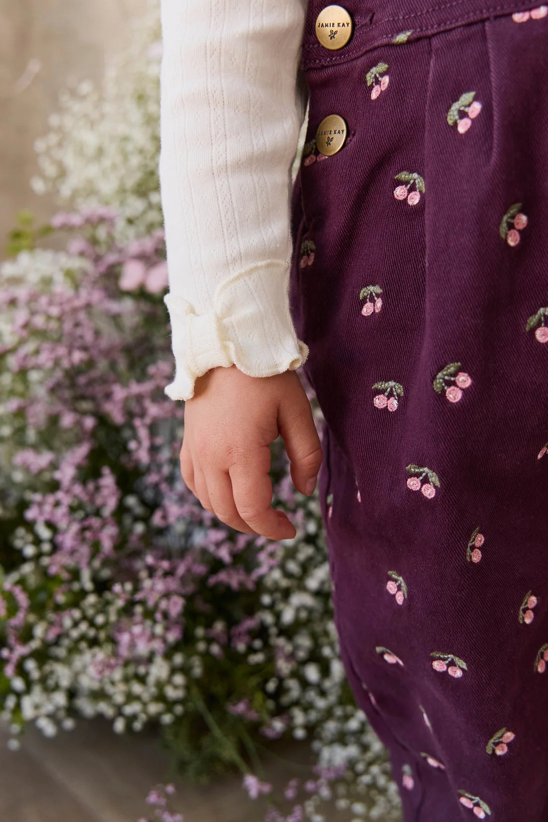 Person wearing a purple dress with floral patterns in front of flowers